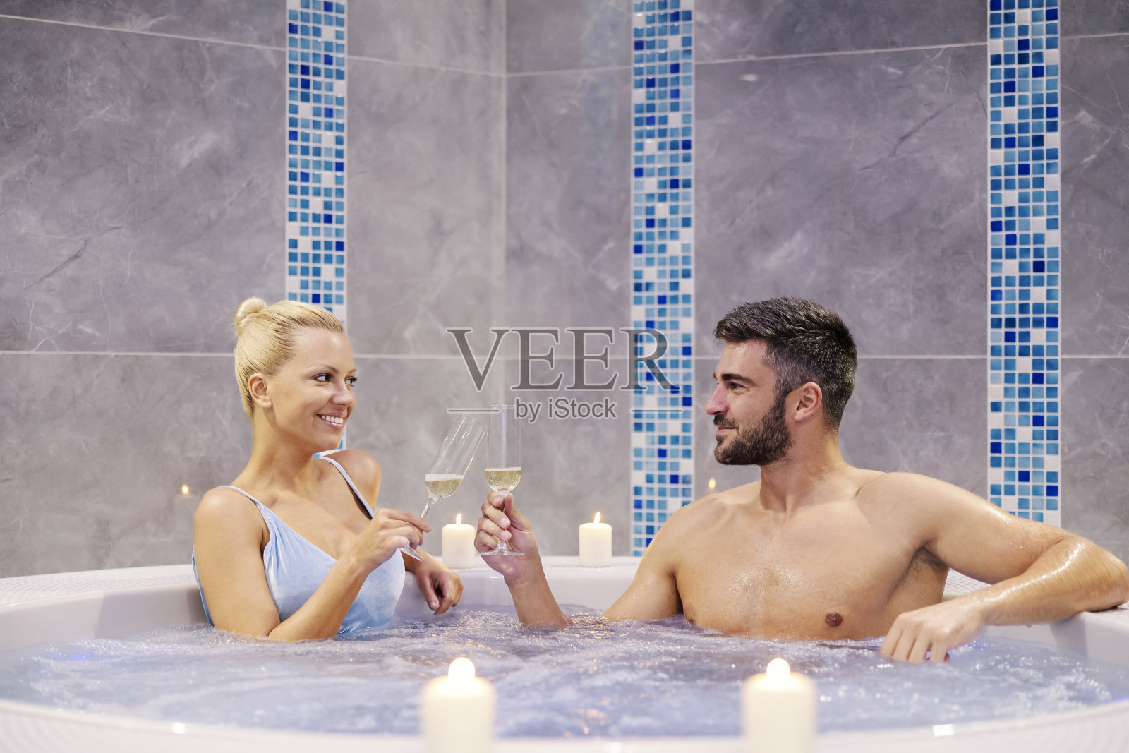 一对浪漫的夫妇在水疗中心喝香槟。一对幸福迷人的夫妇坐在温泉和健康中心的热浴缸里，用香槟或葡萄酒为他们的周年纪念日祝酒。照片摄影图片