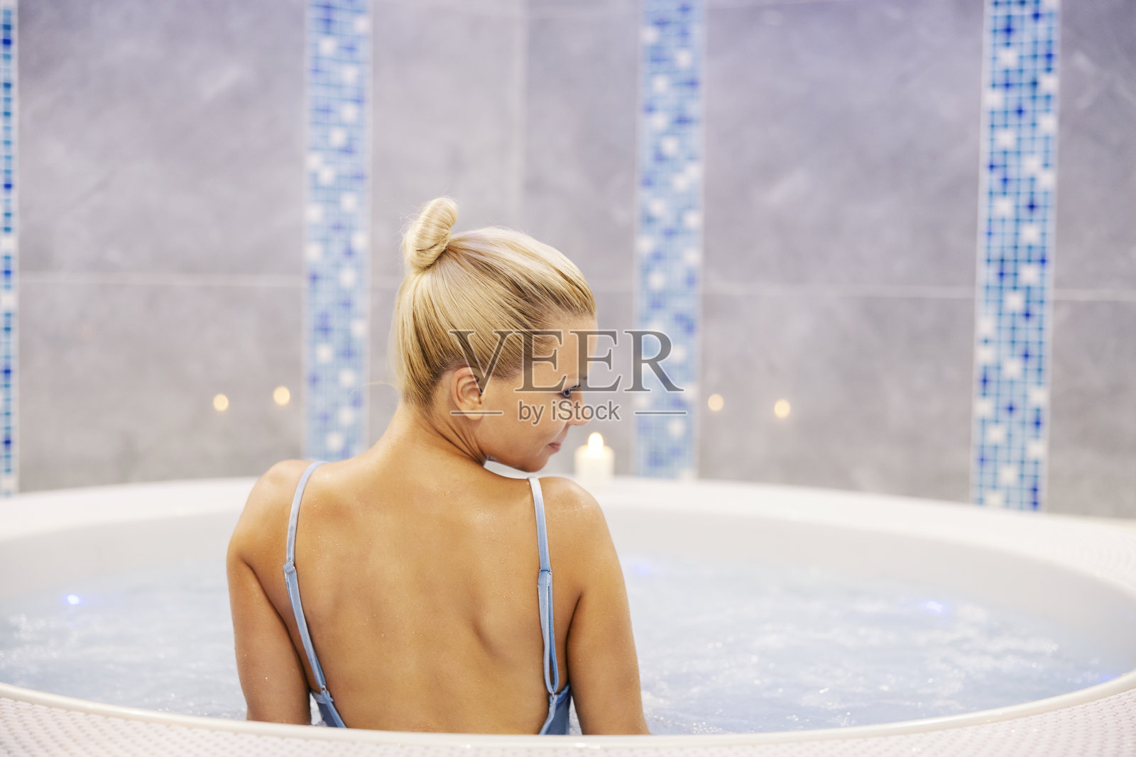 一个女人在水疗和健康中心的热水浴缸里。一个穿着泳装的金发女人正坐在热浴盆里，背朝下，放松着。照片摄影图片