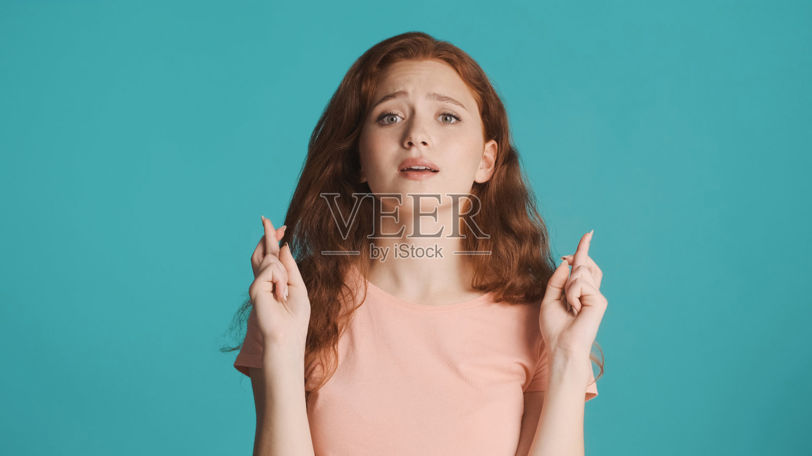 情绪化的红发女孩在彩色背景的镜头前祈祷。请表达照片摄影图片