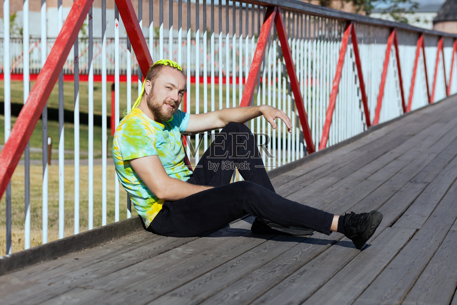 一个留着有趣莫霍克发型的男人坐在桥上，用手遮住眼睛，不让阳光照到他照片摄影图片