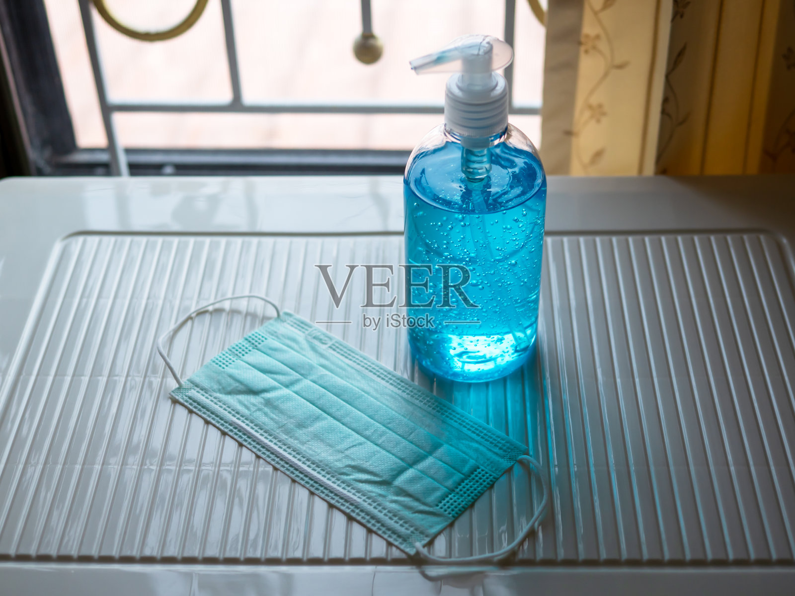 在有窗户背景的房间内使用消毒酒精清洁凝胶、医用冠状病毒口罩、防护新冠病毒。照片摄影图片