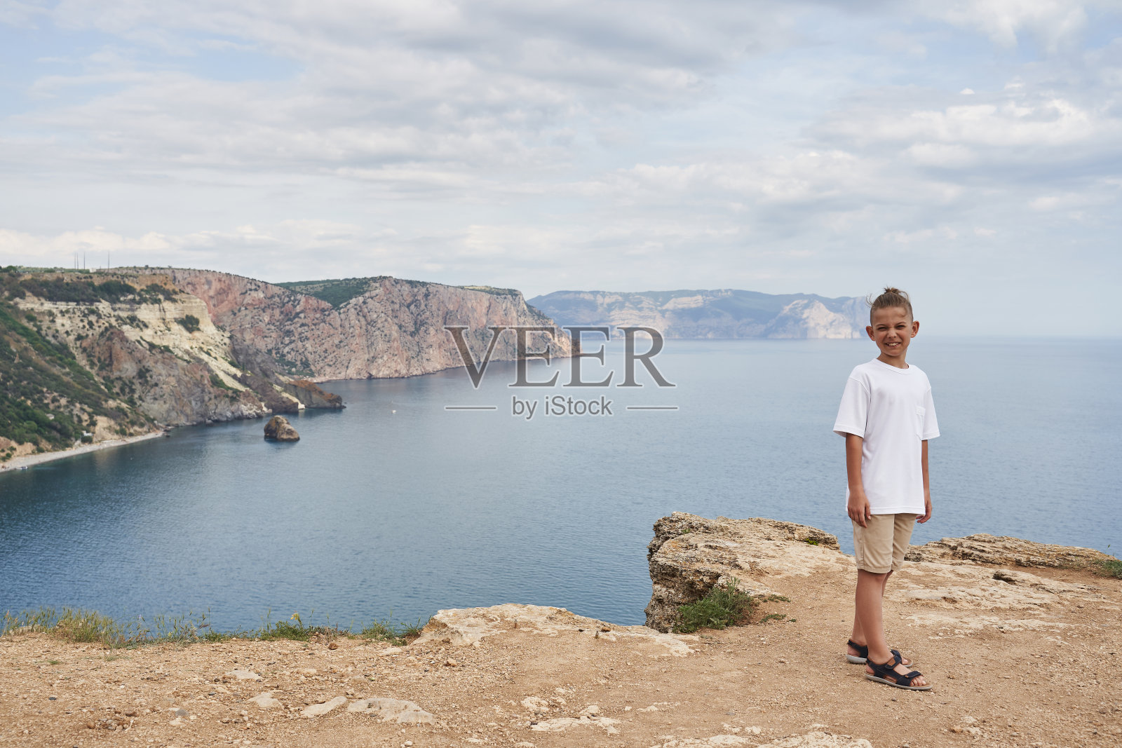 一个穿着轻便衣服的小男孩站在美丽的岩石海岸和美丽的海景的背景下。旅行和冒险照片摄影图片