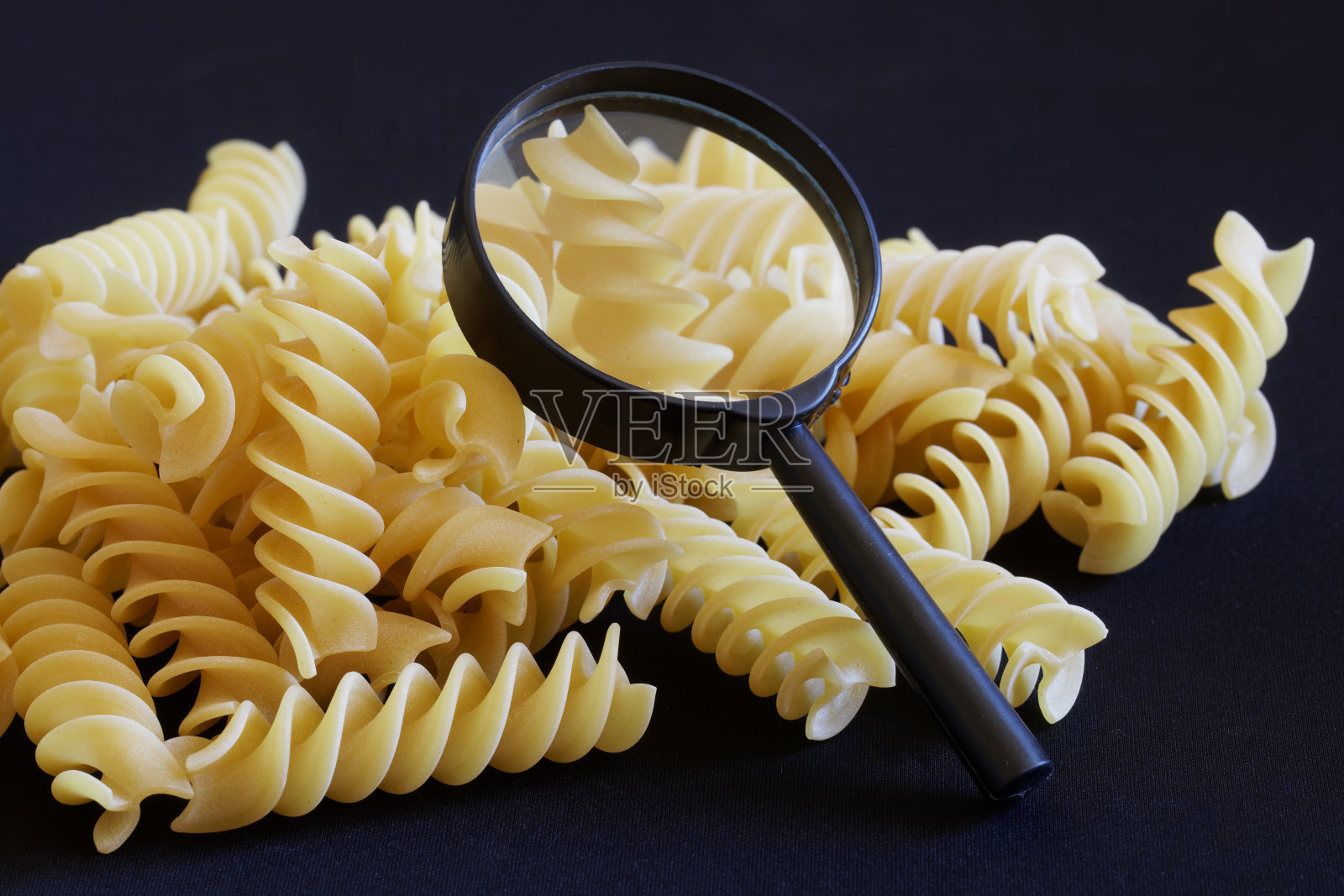 硬质小麦螺旋意大利面和一个放大镜躺在黑暗的背景上。面粉产品质量研究、分析和检验的概念照片摄影图片