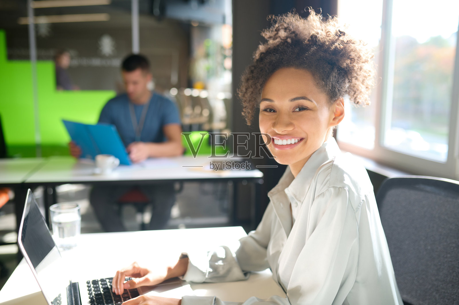 年轻的卷发女职员坐在办公室的桌子旁照片摄影图片