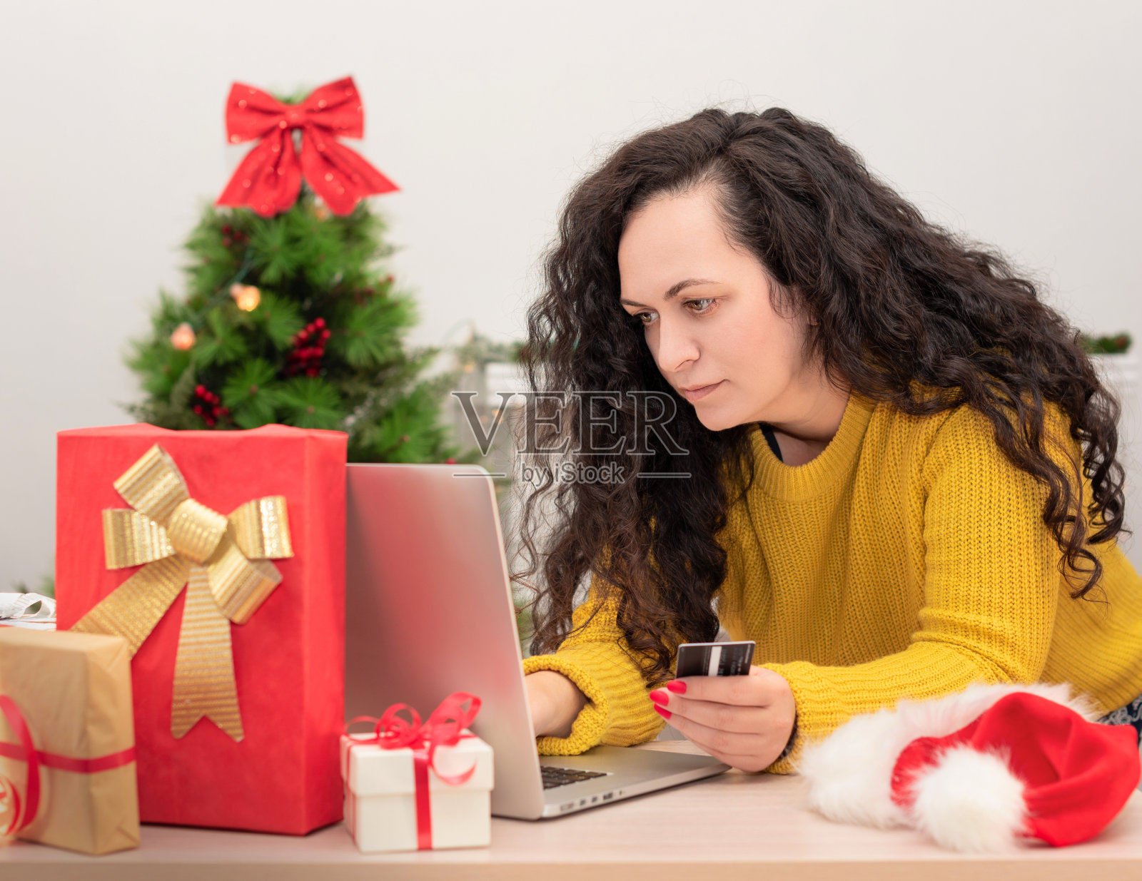 快乐的女人拿着信用卡，在笔记本电脑上购物，背景是圣诞树。圣诞网上购物，准备新年，购买礼物，寒假销售理念照片摄影图片