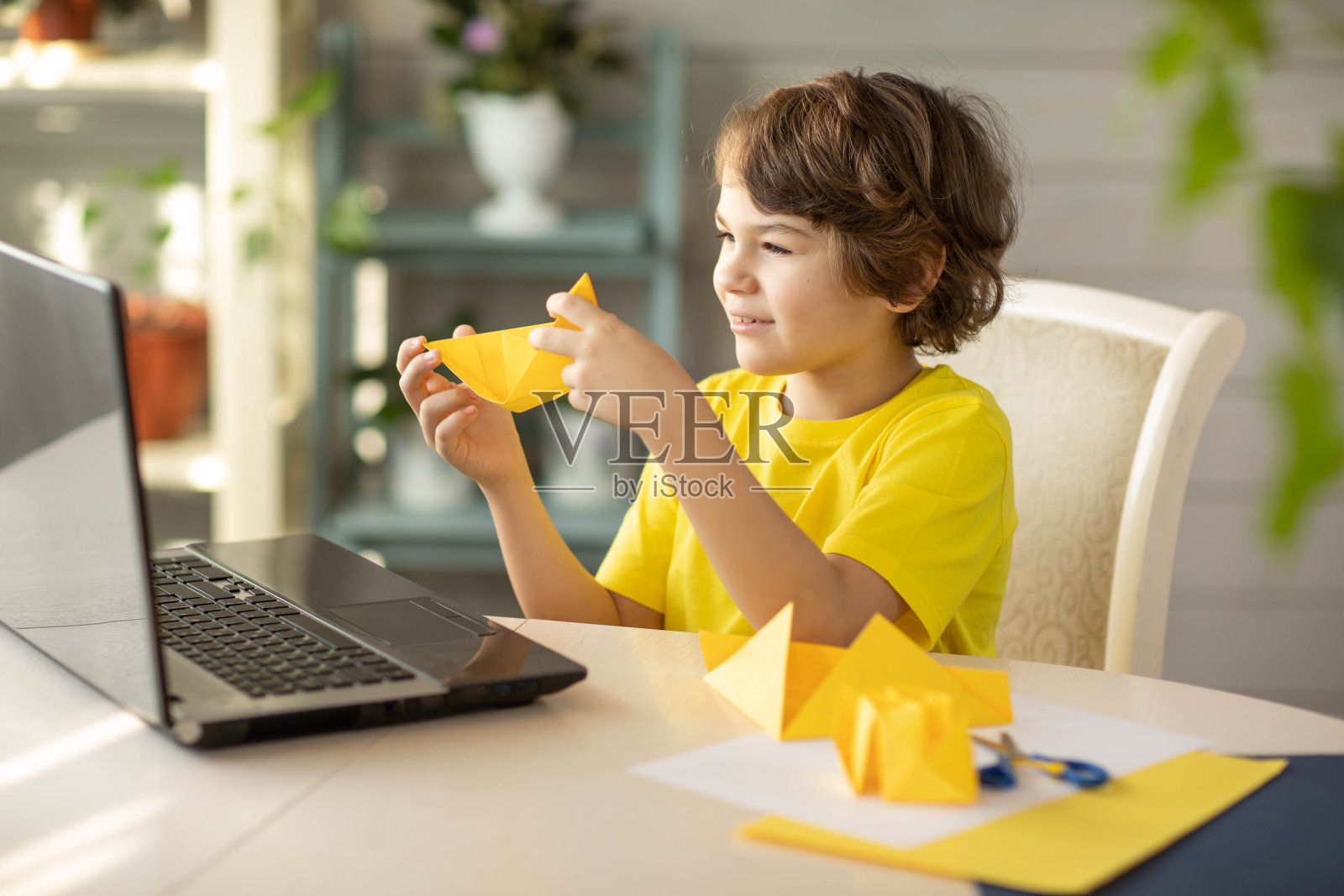 一个穿着黄色t恤的男孩在一个网上折纸工作室，一只纸船照片摄影图片