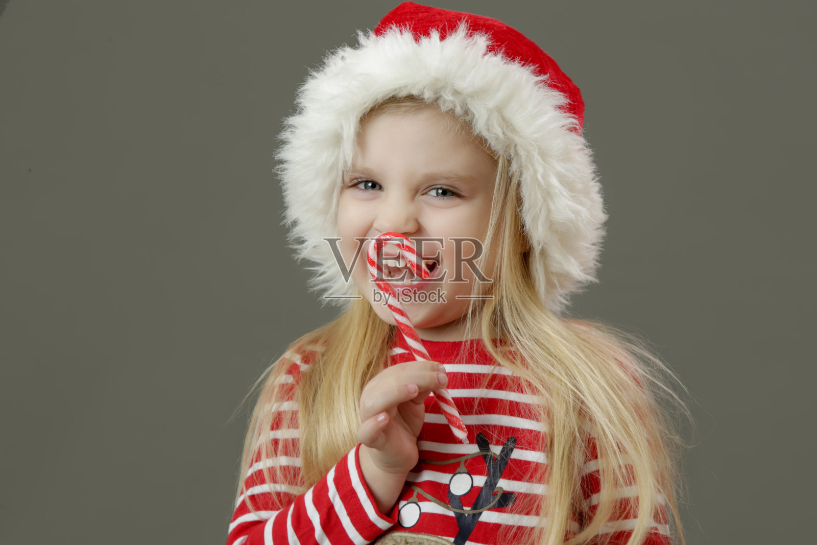4岁的小女孩戴着圣诞帽，手里拿着拐杖糖。这是假期!照片摄影图片