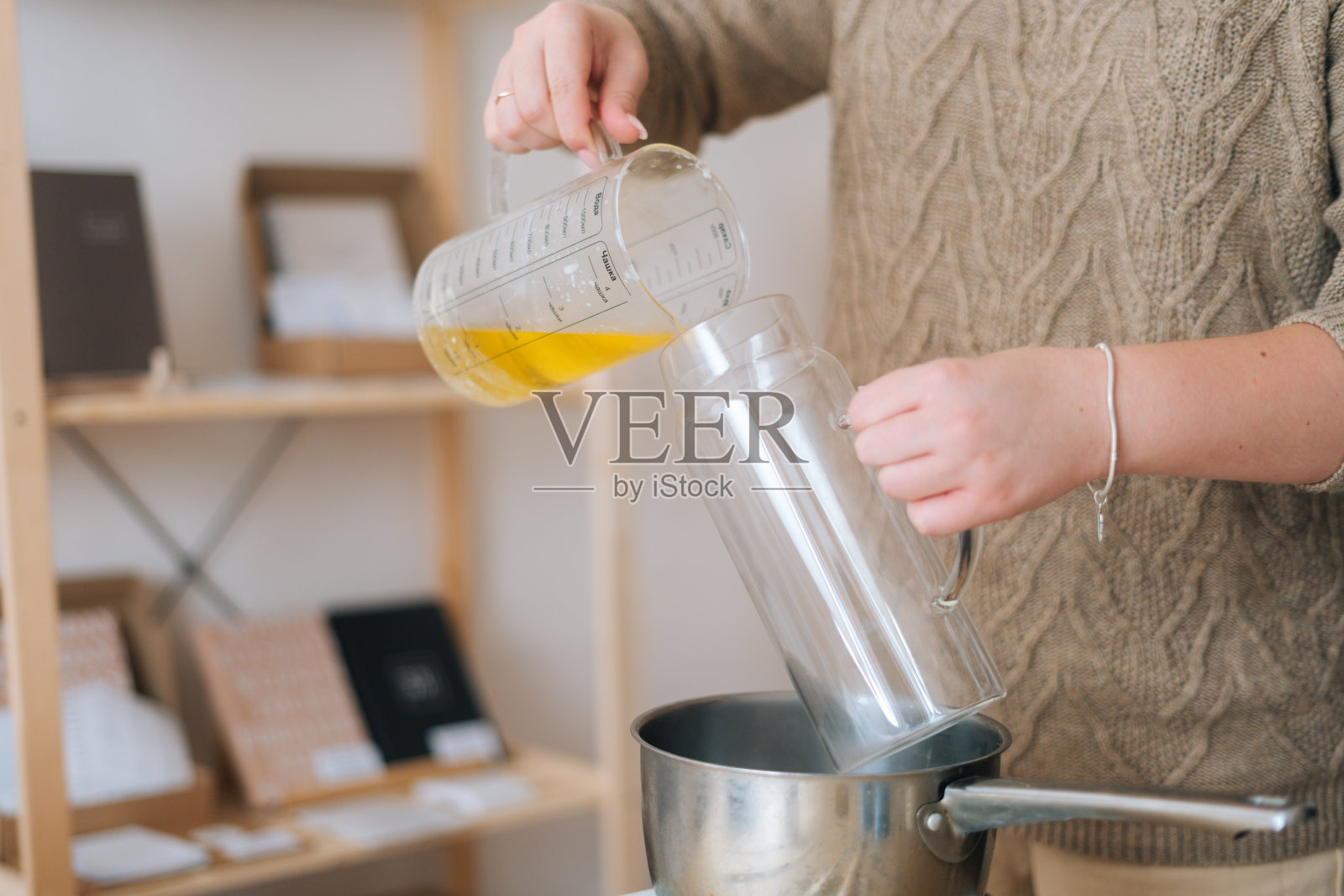 无法辨认的女性工匠的特写镜头融化的蜡倒进玻璃容器创造蜡烛建筑混合物。照片摄影图片