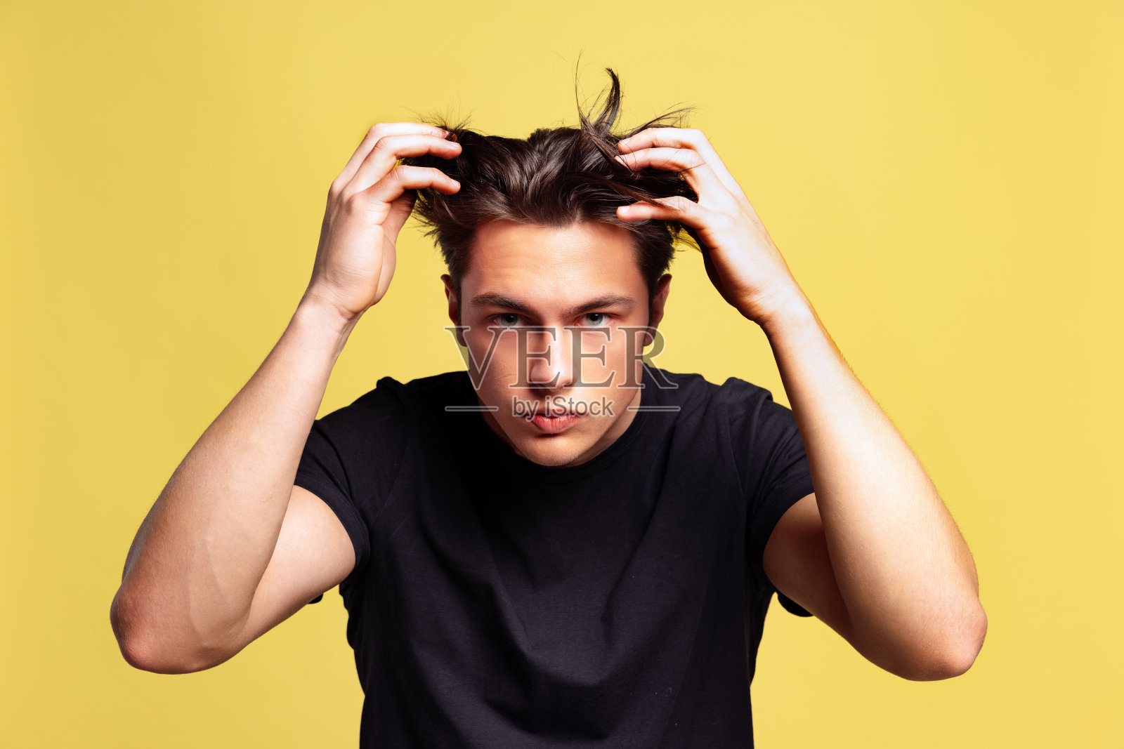 年轻英俊的男子与头发问题的半长肖像孤立在黄色工作室背景。照片摄影图片