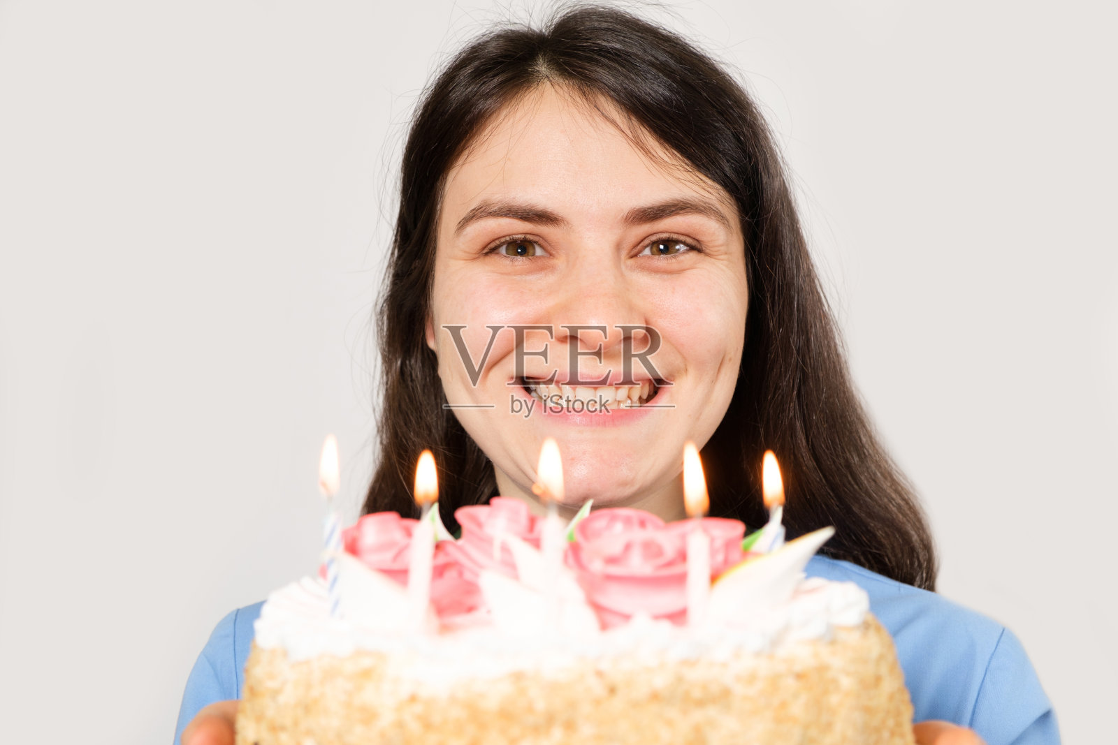 一位身穿蓝色制服的女医生微笑着拿着一个点着蜡烛的生日蛋糕。照片摄影图片