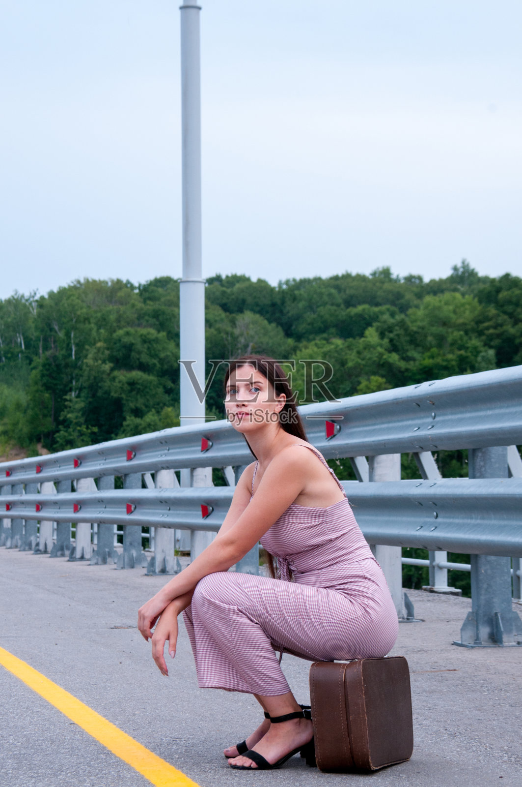 一个女孩坐在空无一人的路边的手提箱上等车照片摄影图片
