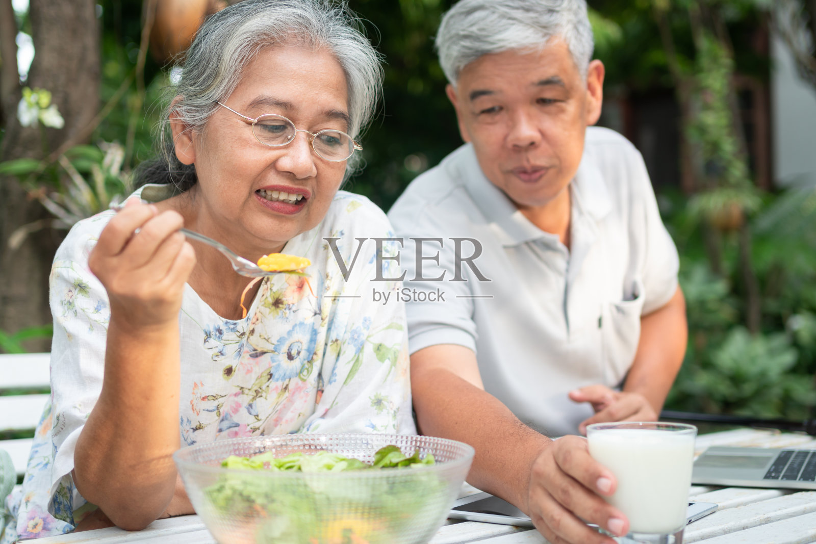快乐的亚洲家庭在后院共进午餐。丈夫喂奶妻子。一个幸福家庭的概念。照片摄影图片