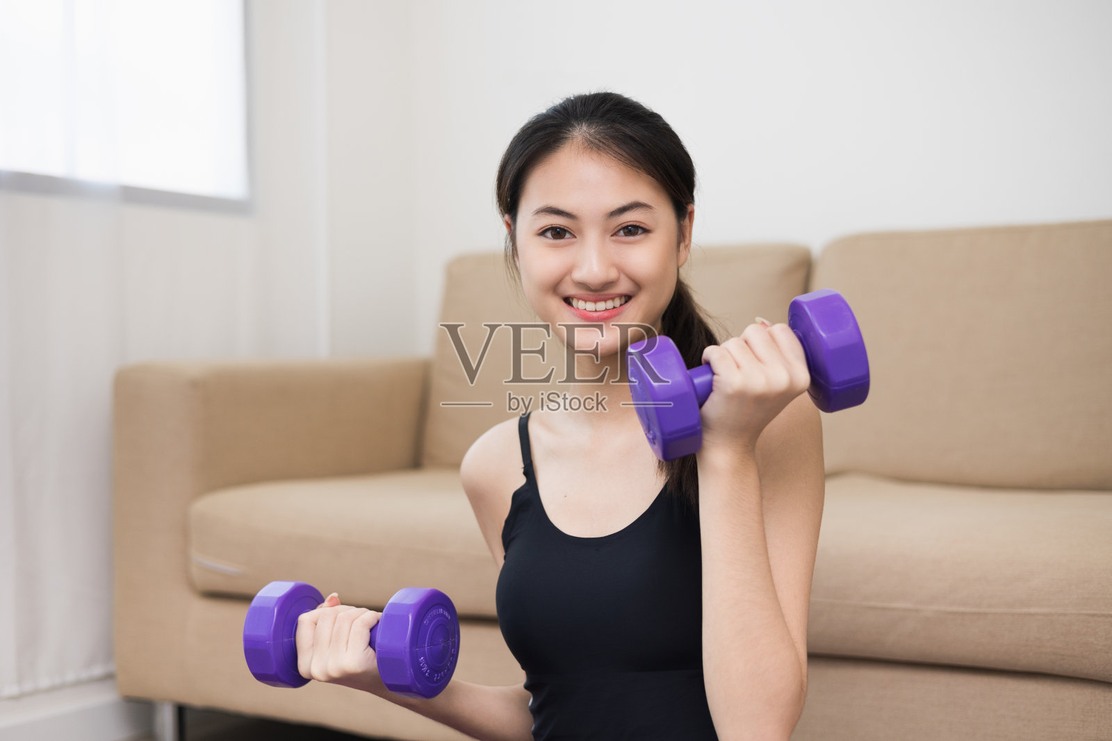 有吸引力的亚洲年轻健身妇女举哑铃重量锻炼在家里的客厅。新鲜感觉的女性训练和锻炼穿着运动服，身体健康。照片摄影图片