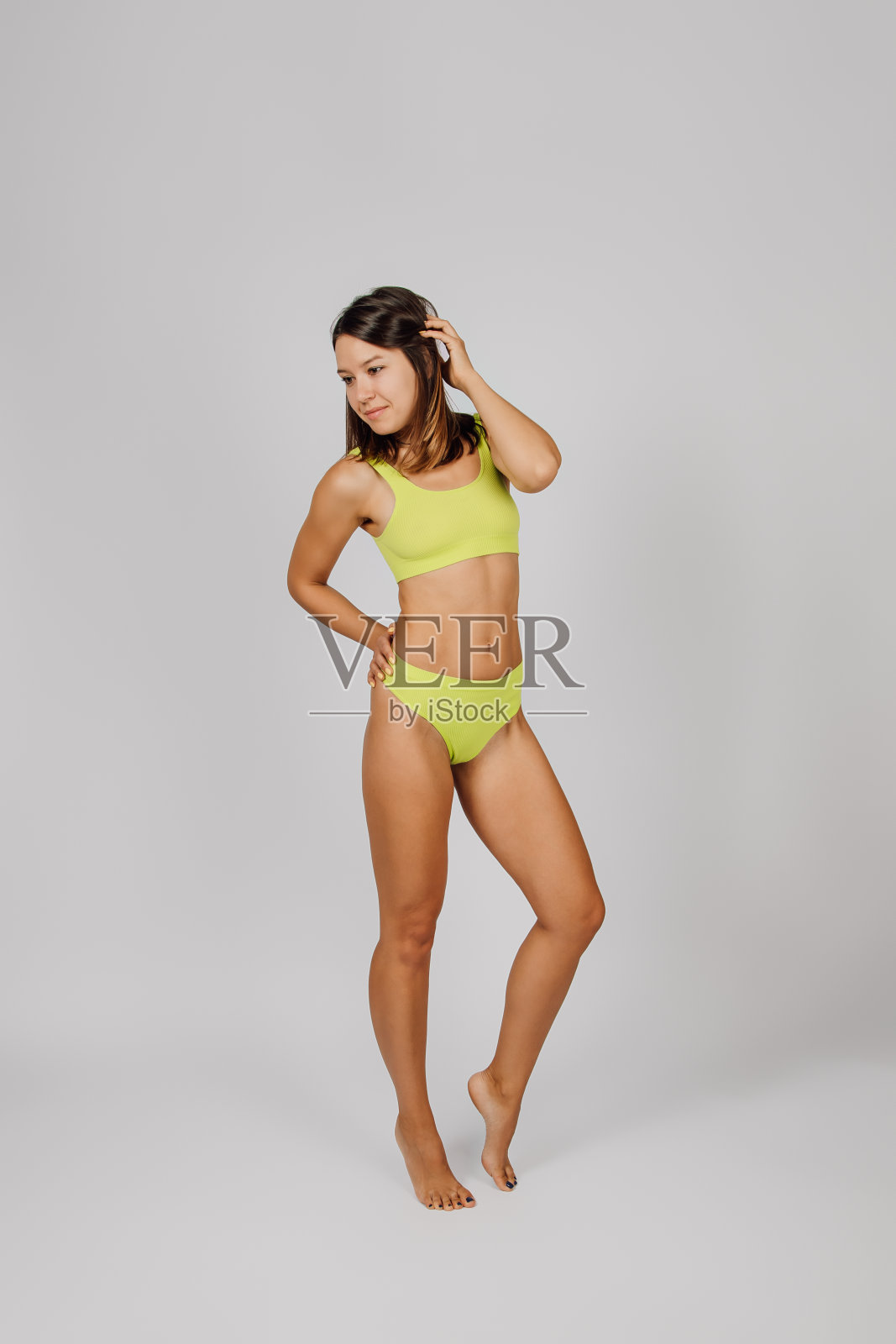 白人女人摆姿势。年轻的褐发女郎在一个孤立的背景下，用她的手握着她的头发，优雅地站着，她穿着黄色的内衣，展示了完美的苗条，健美的身体照片摄影图片