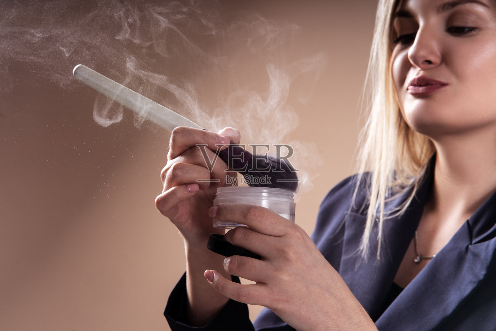 年轻的女化妆师，用刷子和粉化妆。粉在空气中。专业化妆的概念。撅起嘴唇和亲吻的姿势。照片摄影图片