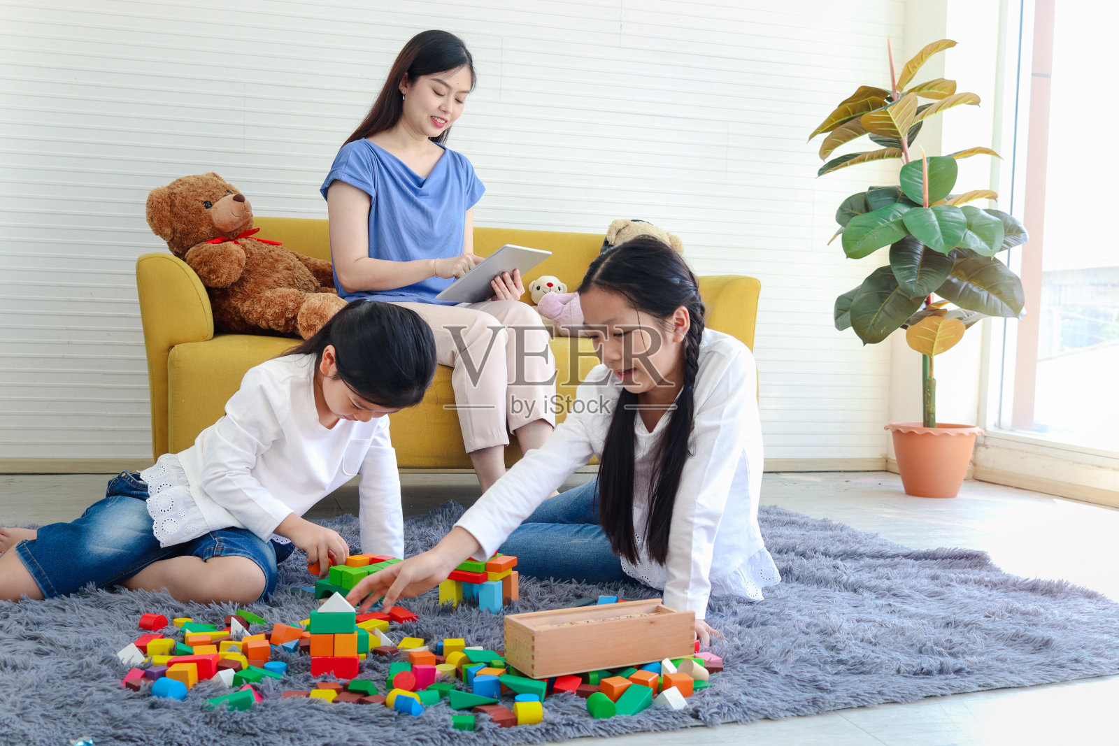 两个女儿在一起玩积木游戏，妈妈坐在沙发上上网，妈妈用平板电脑上网工作，妹妹和孩子在一起消磨时间。照片摄影图片