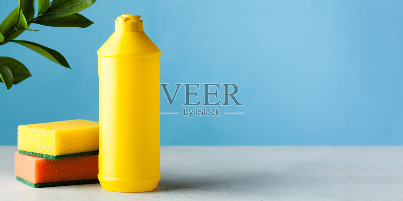 蓝色背景上的黄色瓶子模型，里面有洗洁精和海绵。照片摄影图片