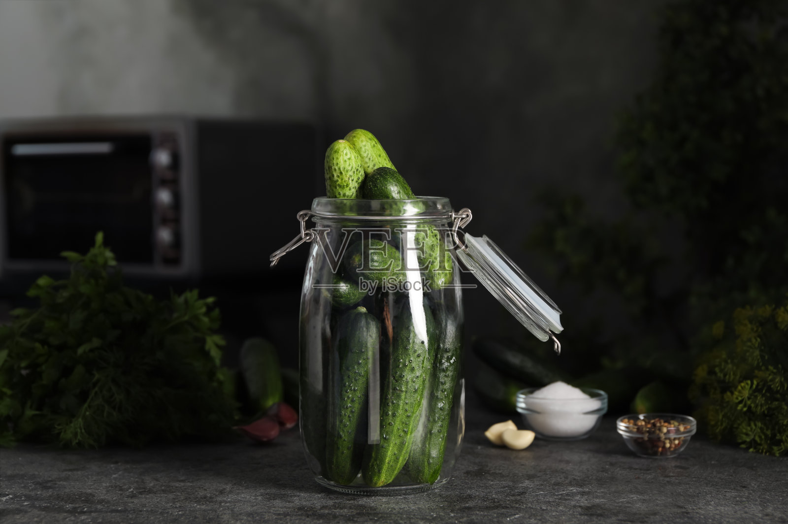深灰色的厨房桌子上放着盛有新鲜黄瓜的腌黄瓜罐照片摄影图片