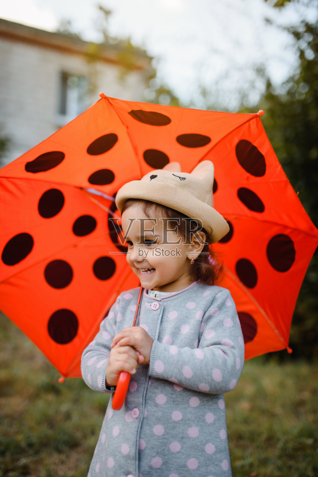 一个快乐微笑的2岁小女孩的肖像，在户外拿着她的红色圆点伞。照片摄影图片