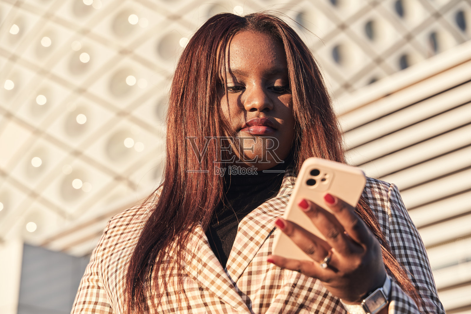 漂亮的非洲裔美国妇女的肖像，穿着西装浏览互联网，更新应用程序，使用免费的wi-fi电子设备。年轻女孩用手机打字照片摄影图片