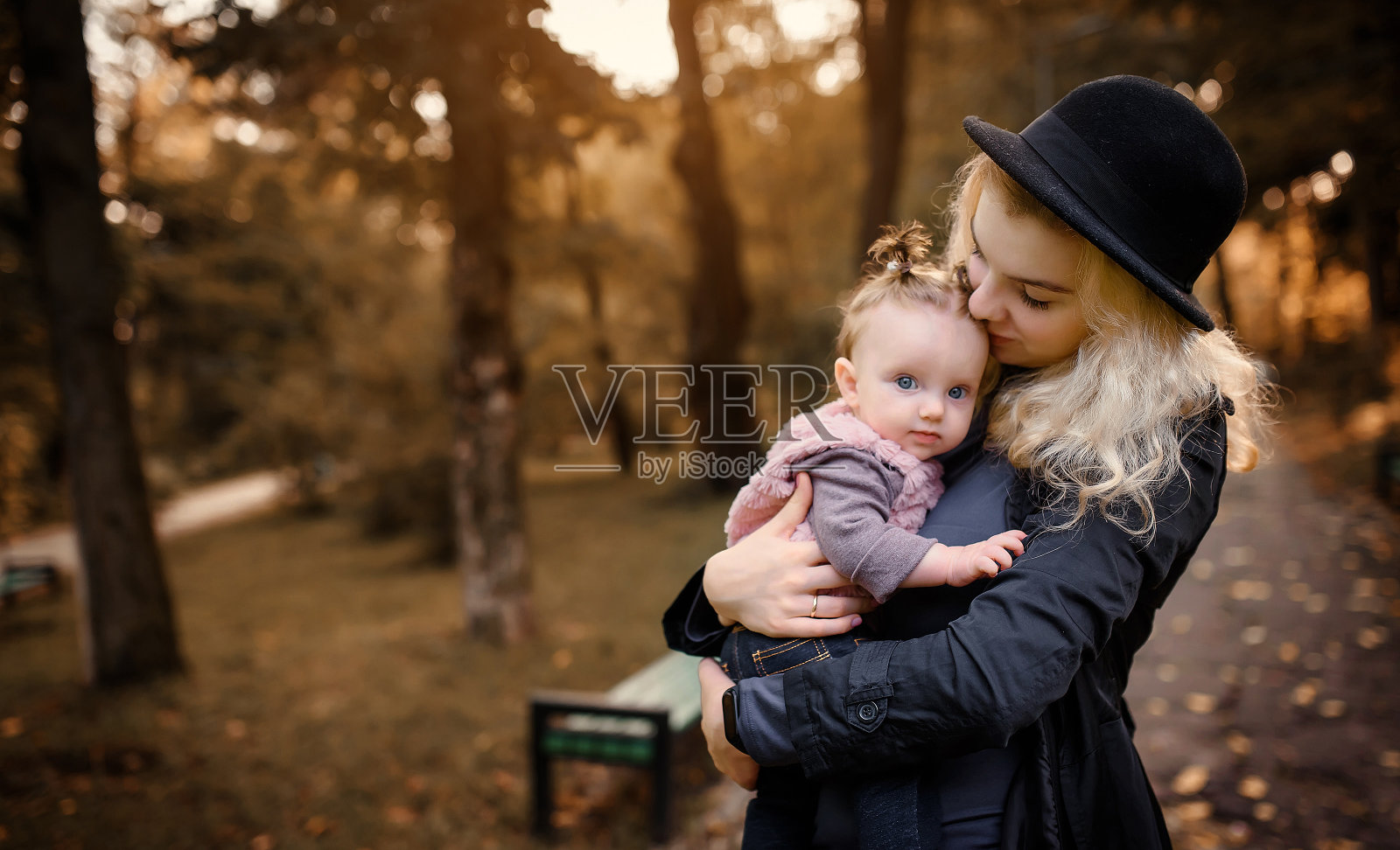 在秋天的公园里，一位年轻的母亲抱着她6个月大的女儿。照片摄影图片