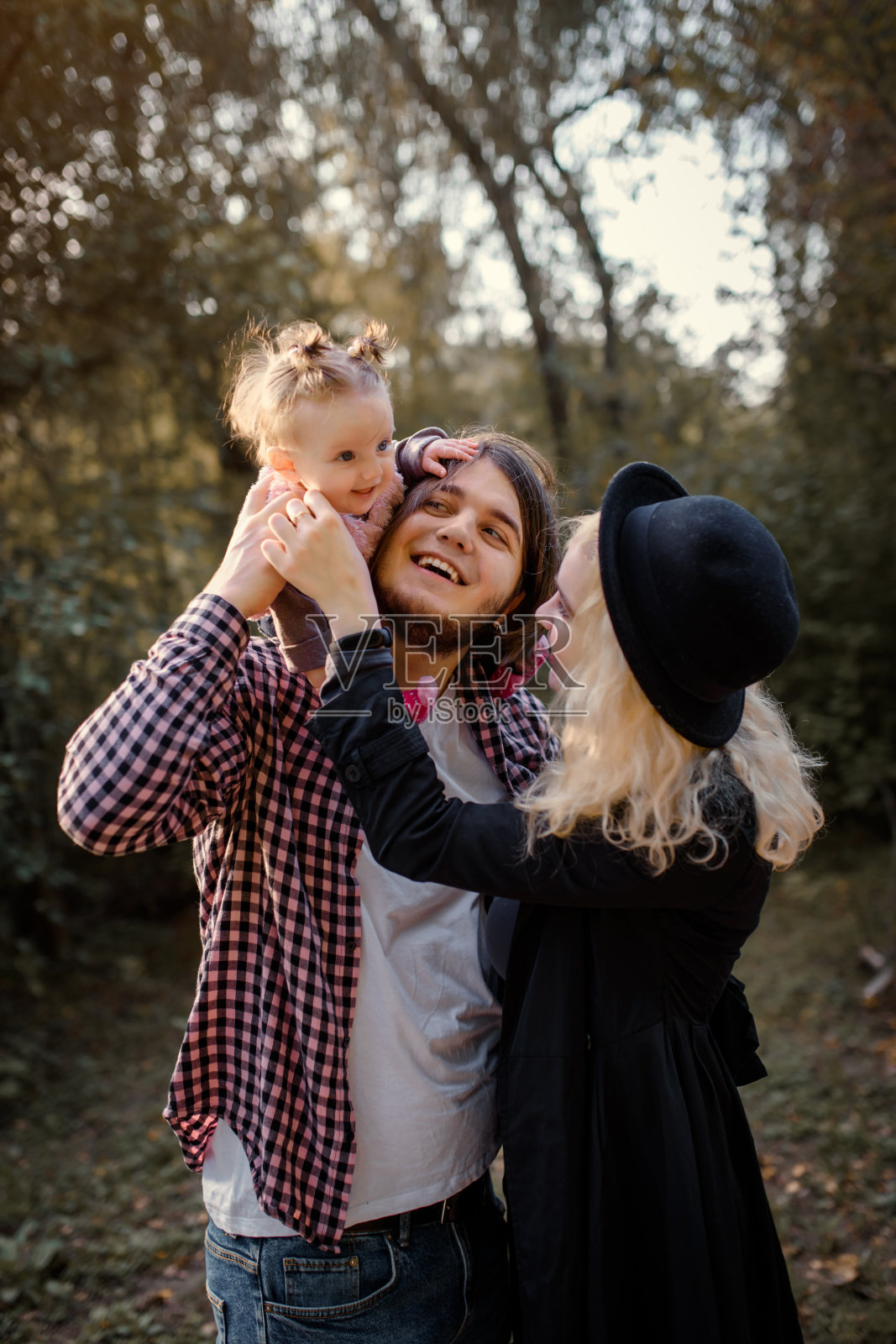 幸福微笑的一家人正在秋天的公园里散步。一个6个月大的女婴正坐在爸爸的肩膀上和妈妈在秋天的公园里玩耍。照片摄影图片