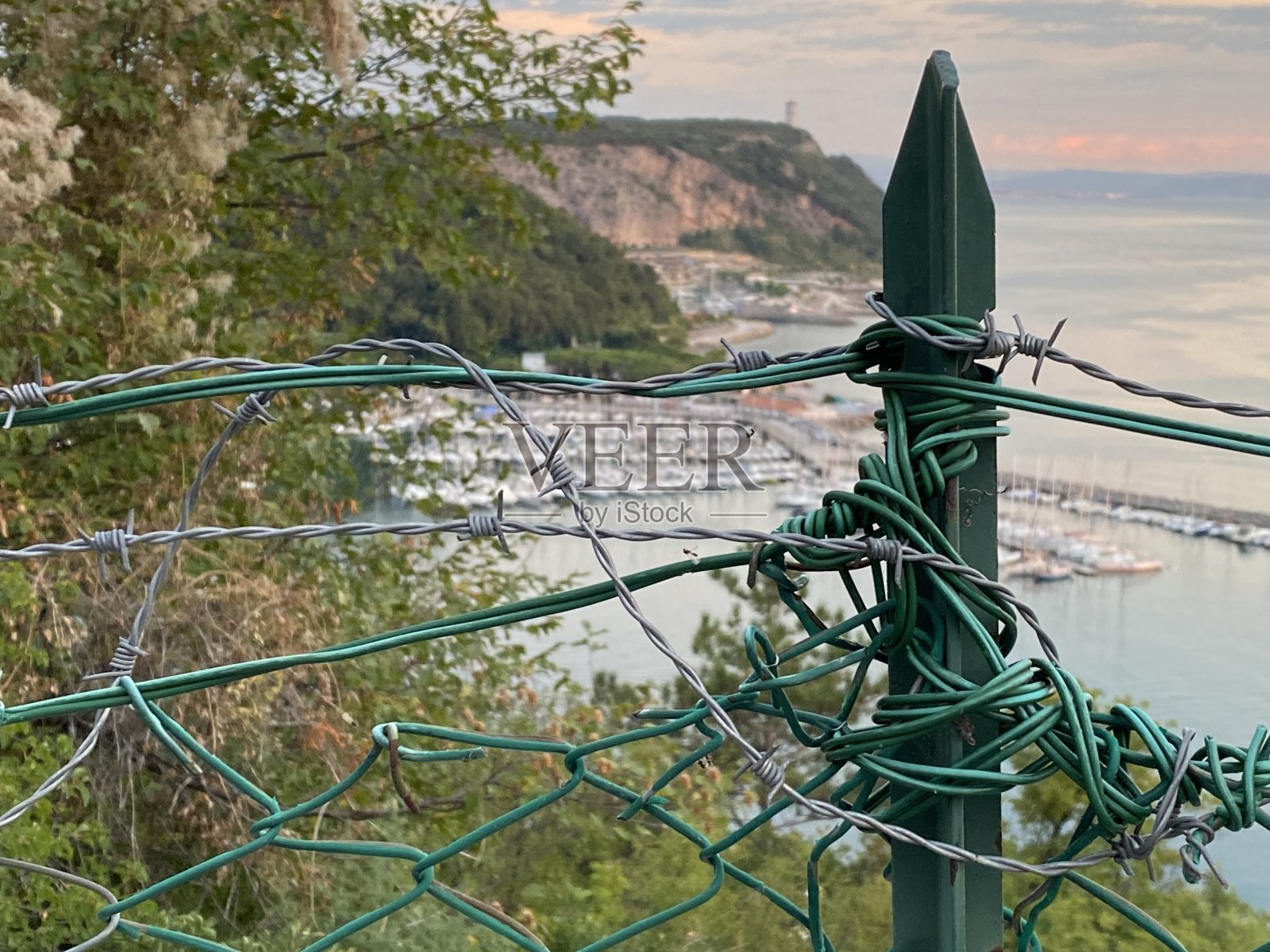 位于意大利弗ulii - venezia Giulia地区Duino和Trieste之间的Sistiana - Portopiccolo在日落时和铁丝网的铁链围栏照片摄影图片