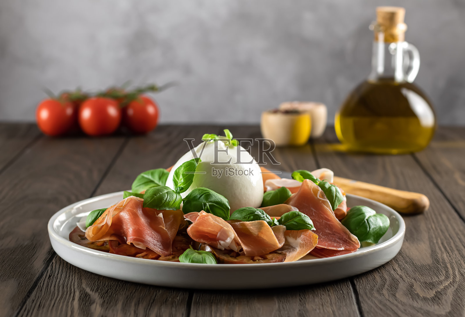 精选意大利熏火腿配布拉塔奶酪，新鲜罗勒，番茄和橄榄油。浅景深。照片摄影图片