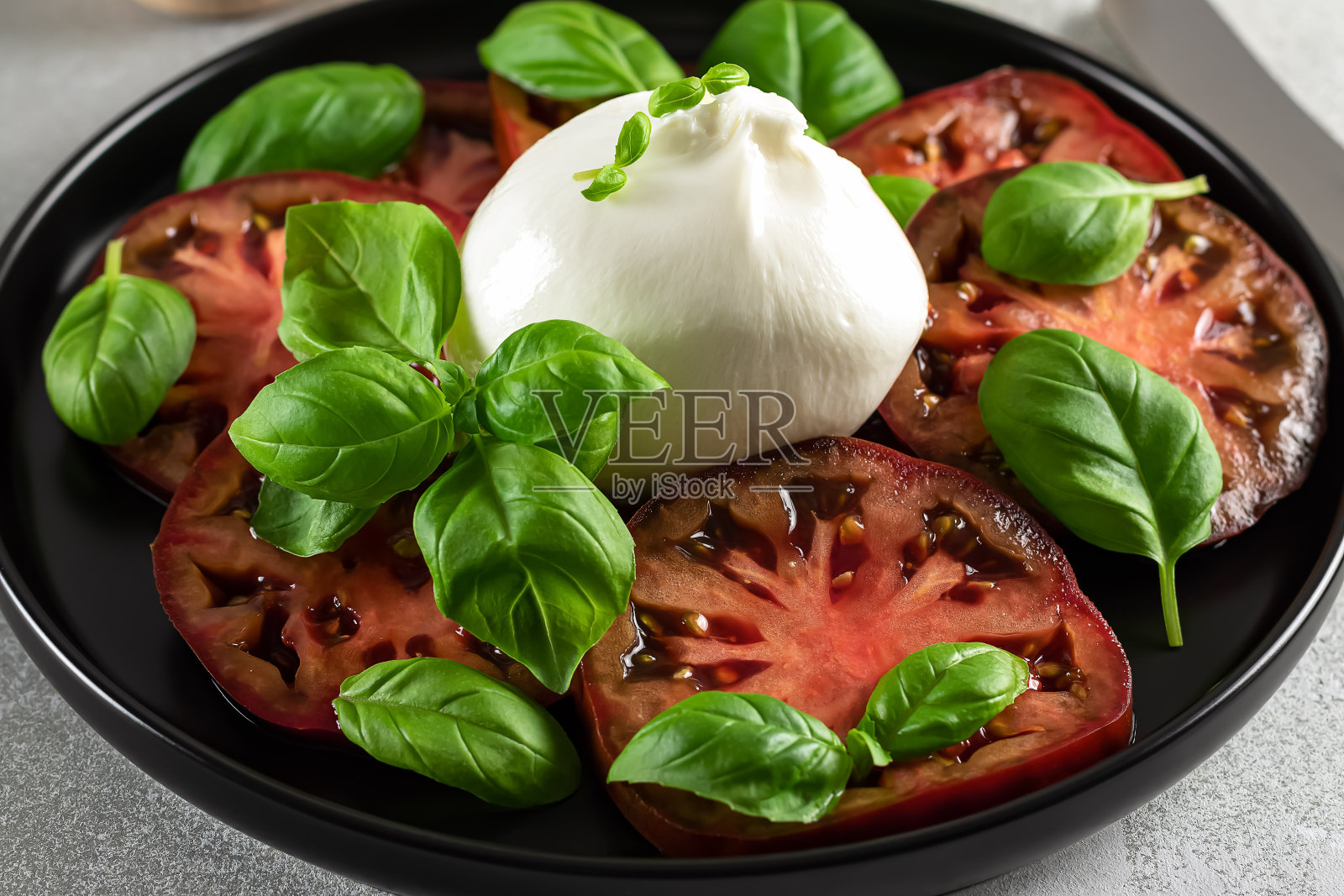 素食开胃菜的特写。番茄和布拉塔奶酪配新鲜罗勒。照片摄影图片