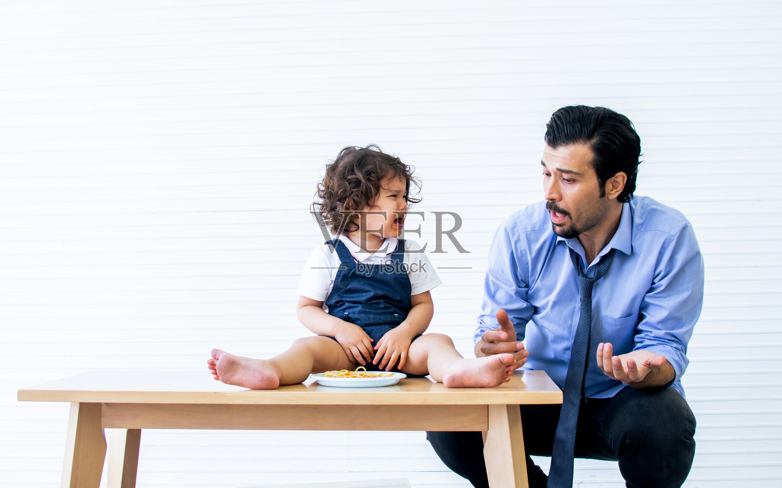 白种人胡子英俊的父亲努力照顾和给他可爱的女儿意大利面早餐。他上班前她又哭又恼。儿童、情感与教育理念。照片摄影图片