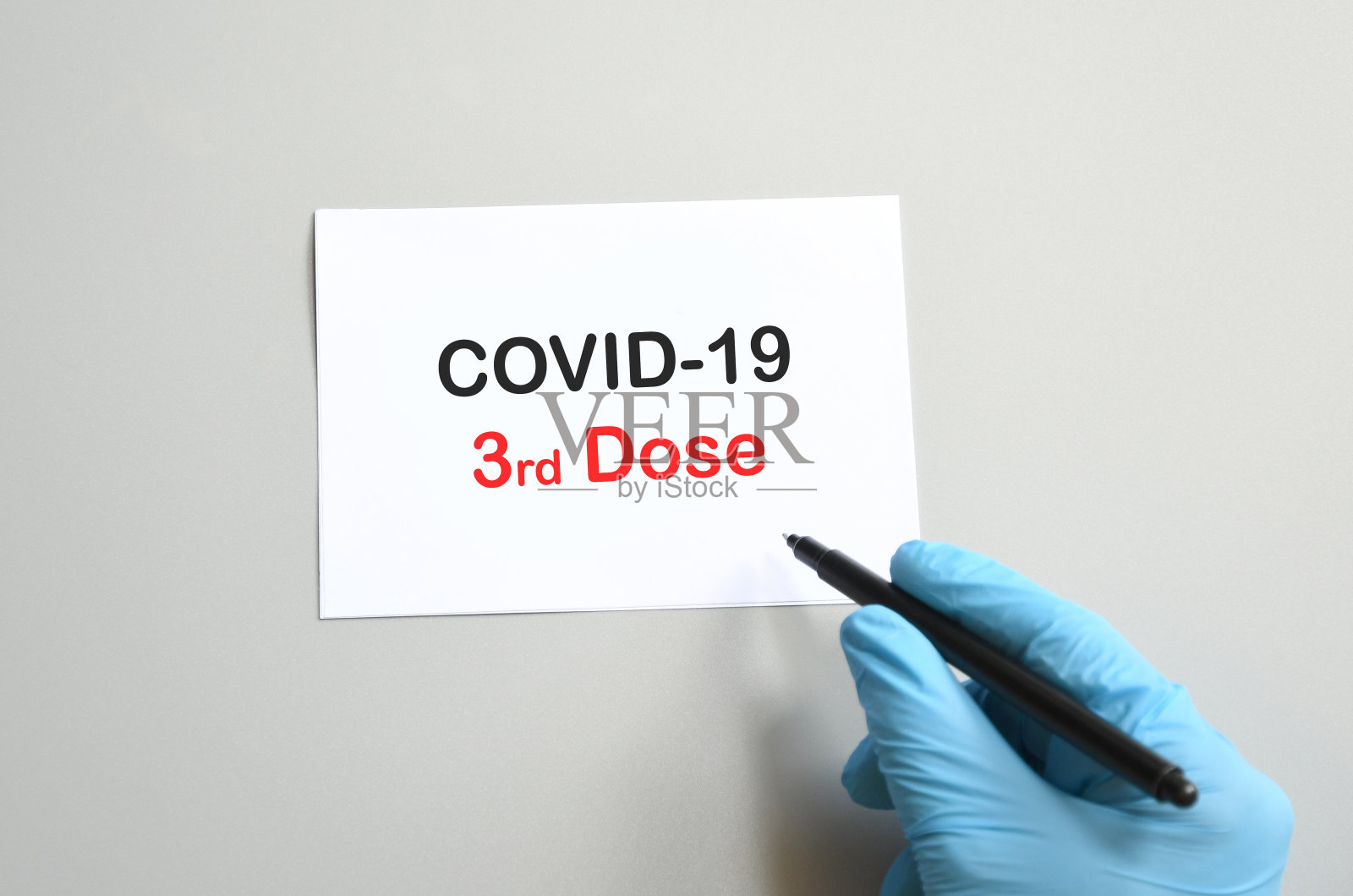 戴蓝色手套的医生的手在白纸上写着“Covid-19第三剂”。使用第三剂疫苗抗击COVID-19病毒的概念。照片摄影图片