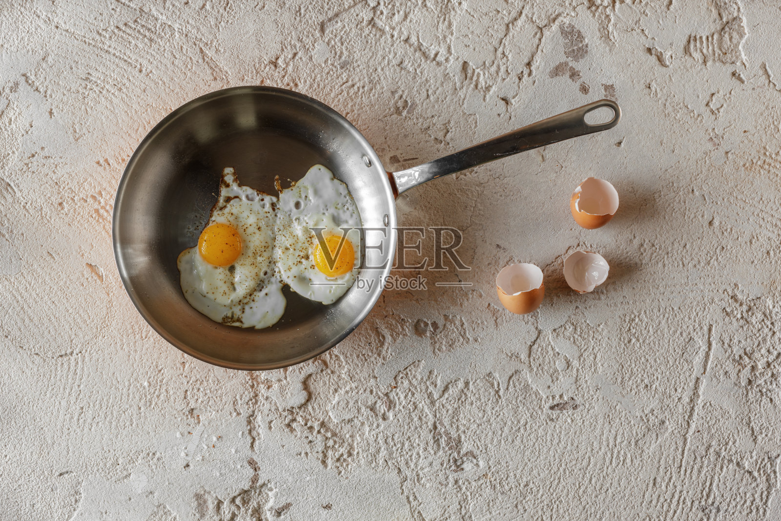 在粗糙的粘土背景下，用铜锅煎两个鸡蛋。健康的早餐概念。健康的早餐概念。照片摄影图片