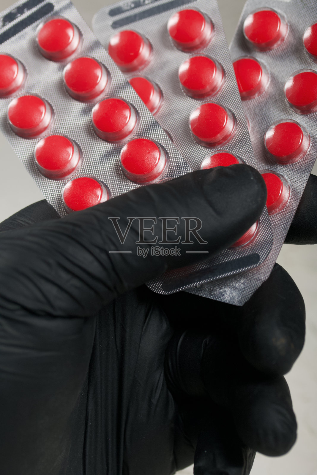 戴着橡胶手套的手拿着红色药丸，水泡起了。在浅色的背景上。特写镜头。照片摄影图片