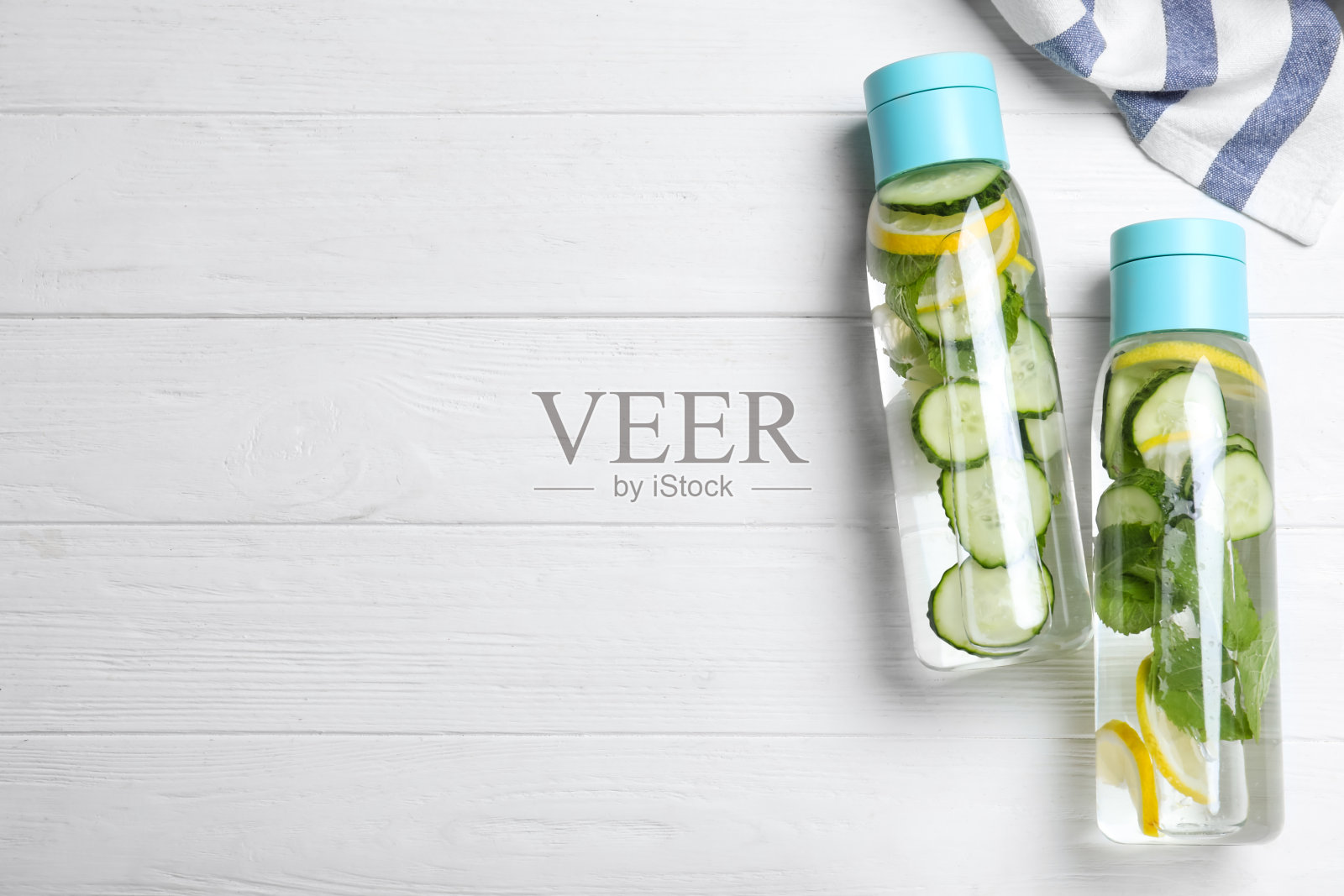 白色木桌上平放着几瓶黄瓜、柠檬和薄荷水。空间的文本照片摄影图片