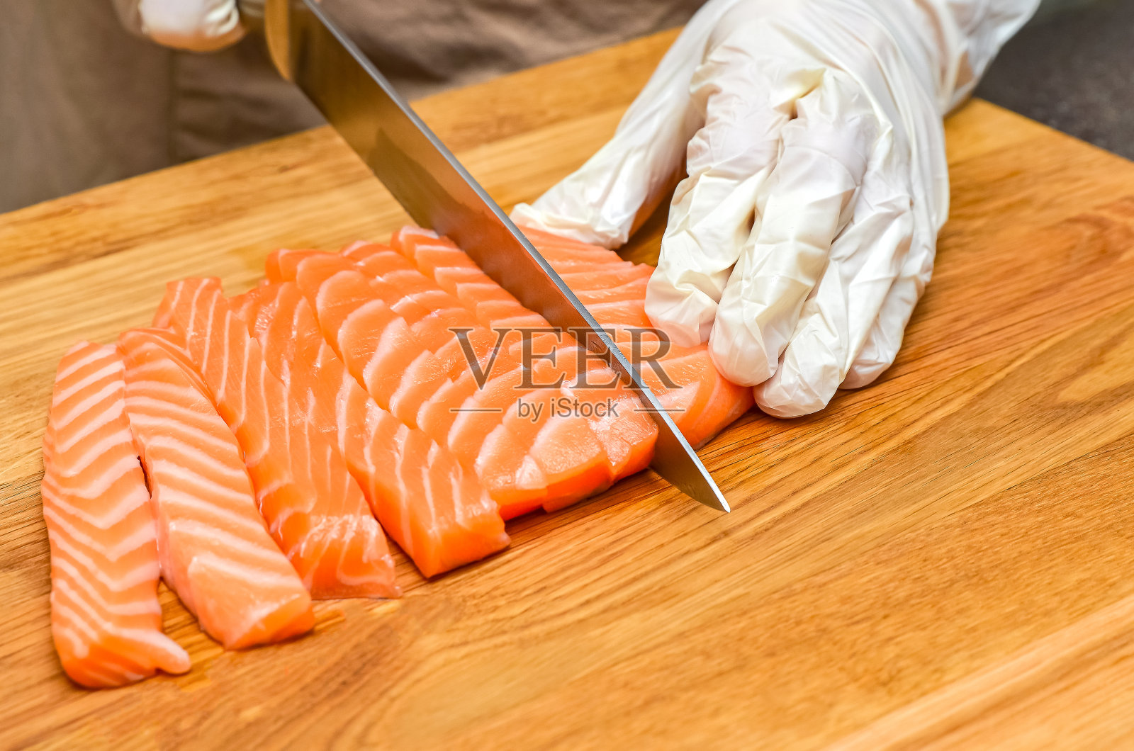 厨师的手合上了。在一块木制的切菜板上，厨师用刀切一条红色的鱼照片摄影图片