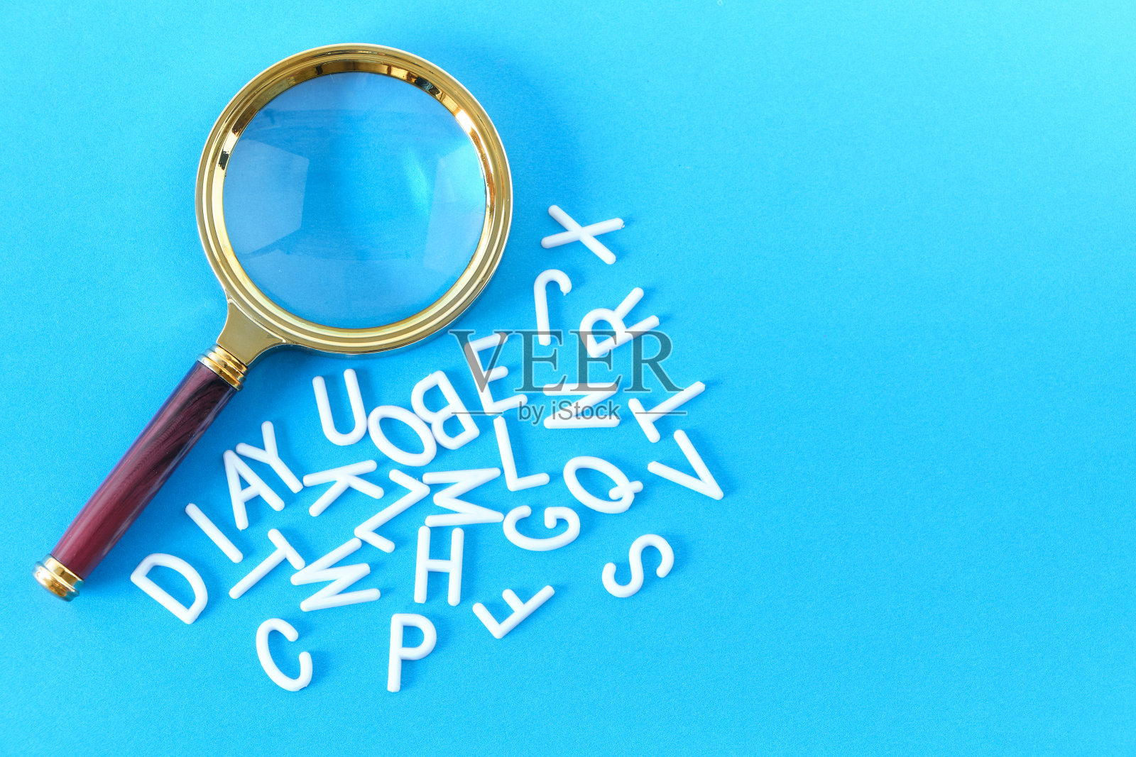 放大镜上蓝色的背景上散落着字母。照片摄影图片