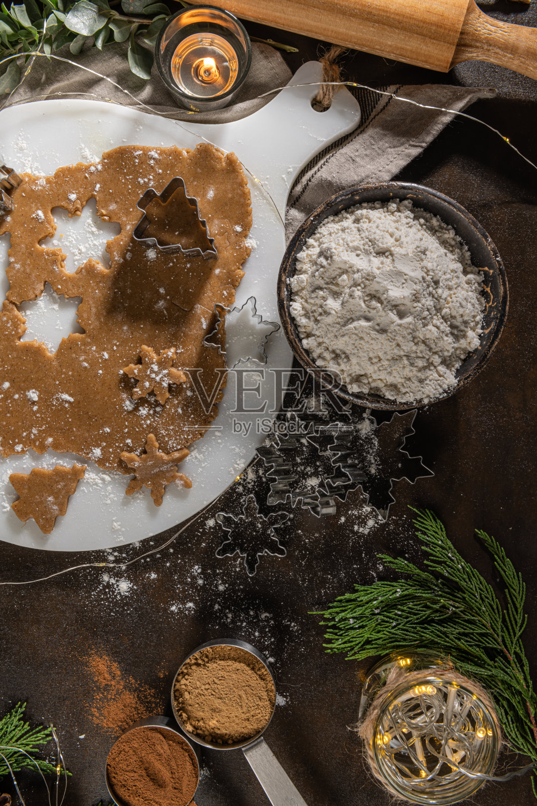 做圣诞姜饼饼干。生面团的形状姜饼人，圣诞树，星星，雪花在纸上托盘，在乡村的桌子上用擀面杖。准备烤照片摄影图片