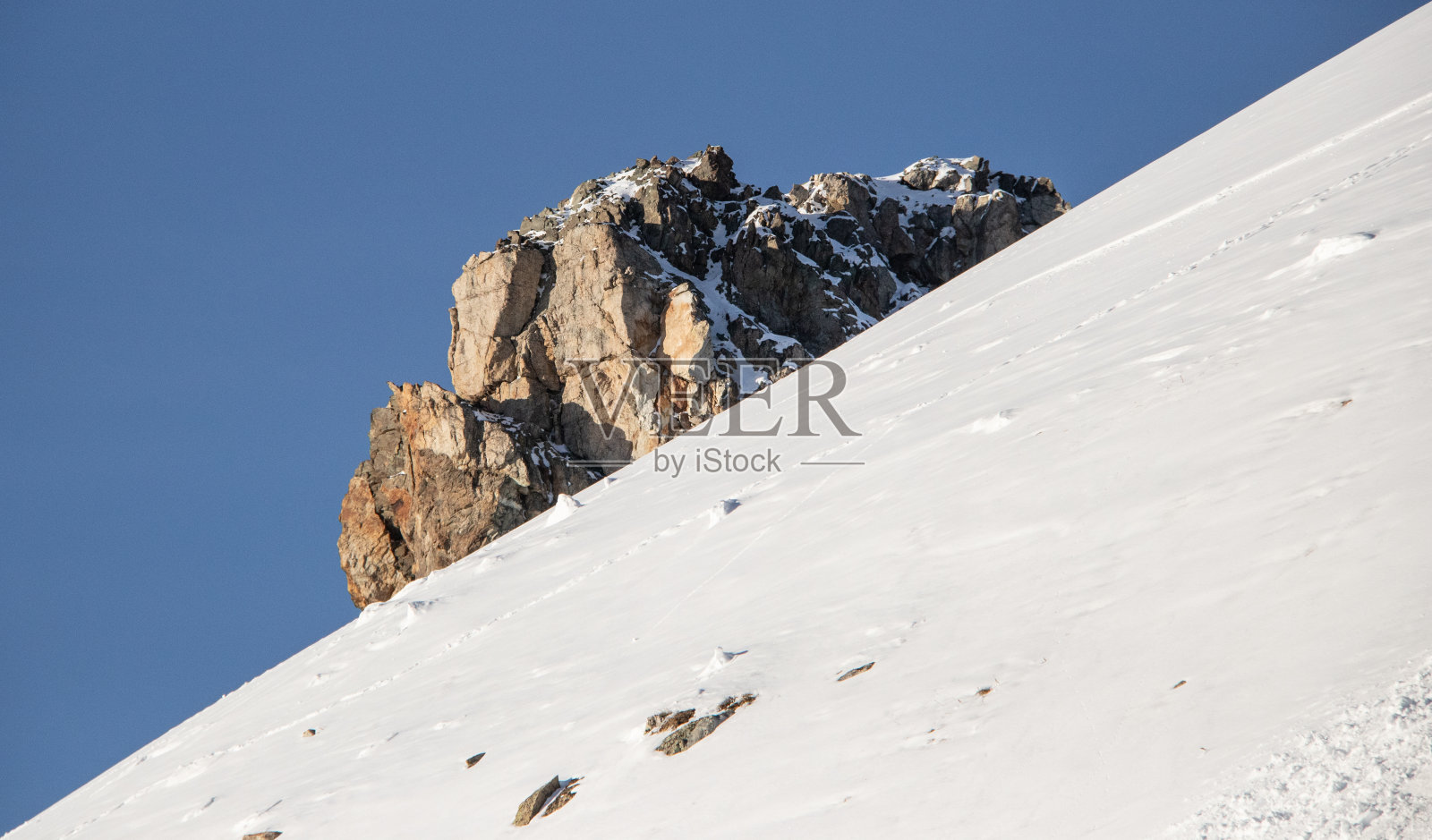 一块大石头在雪山和蓝天的斜坡上照片摄影图片