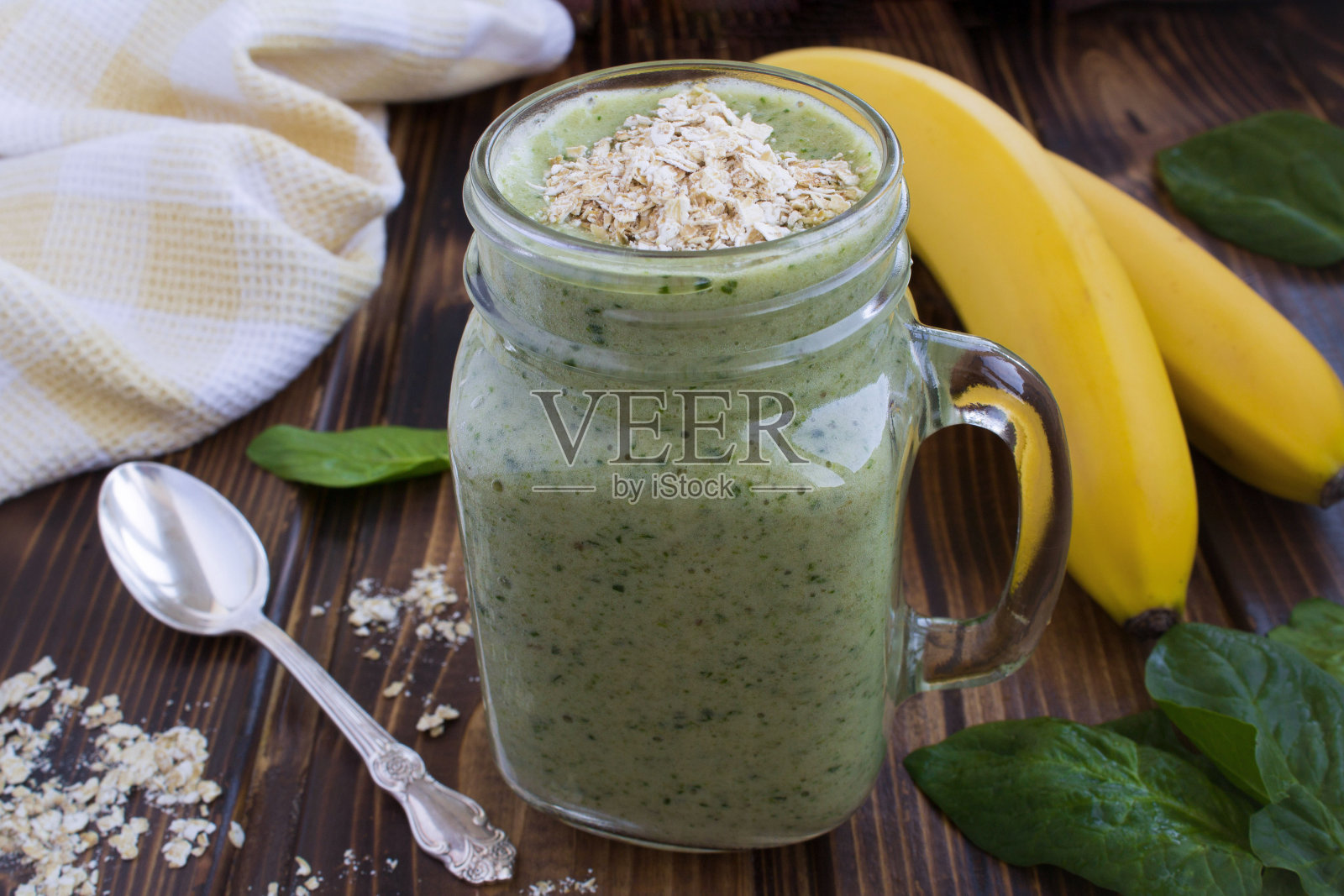 棕色木质背景上的香蕉、菠菜和燕麦片奶昔。特写镜头。照片摄影图片