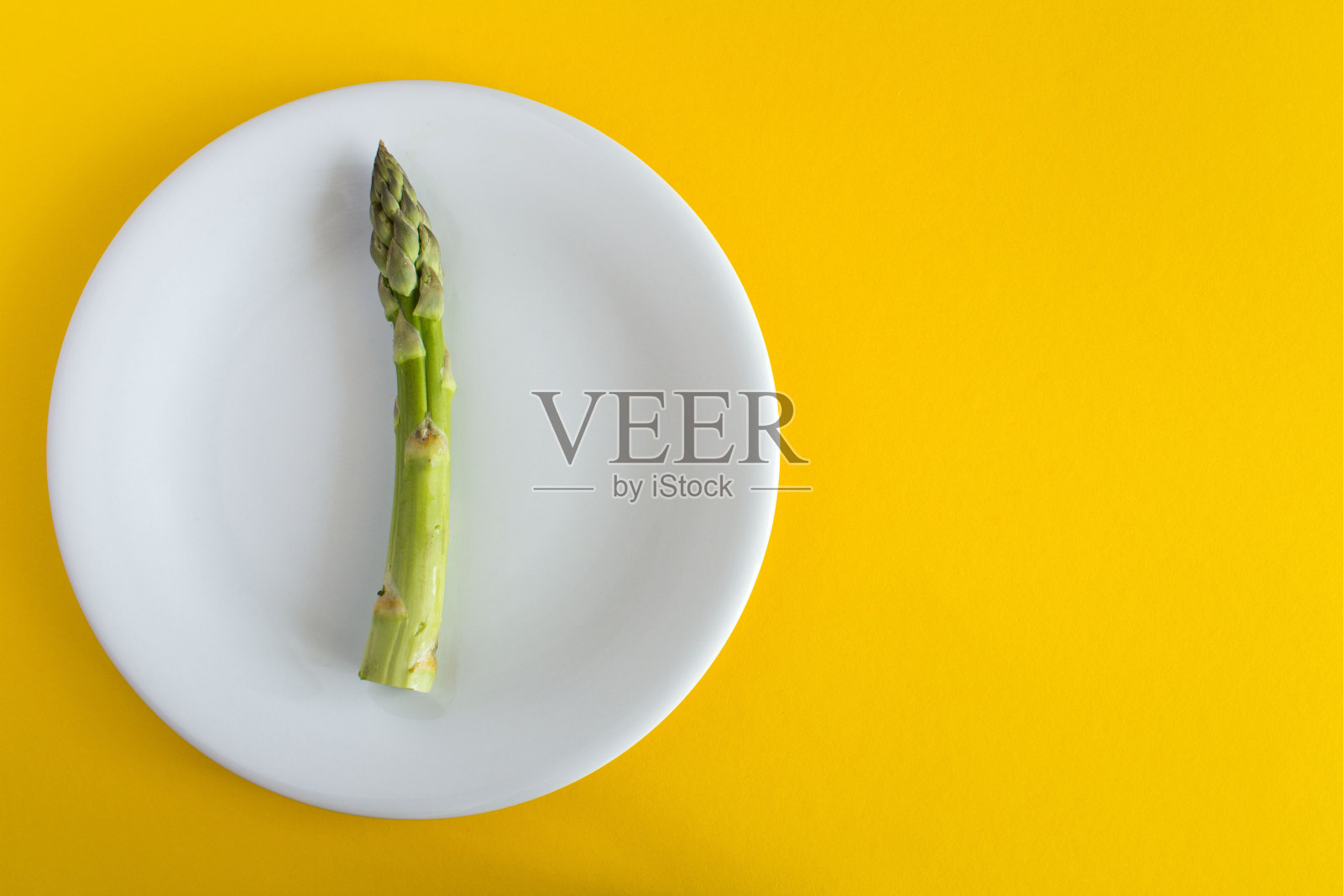 黄色背景上白色盘子里的生芦笋。前视图。副本的空间。照片摄影图片