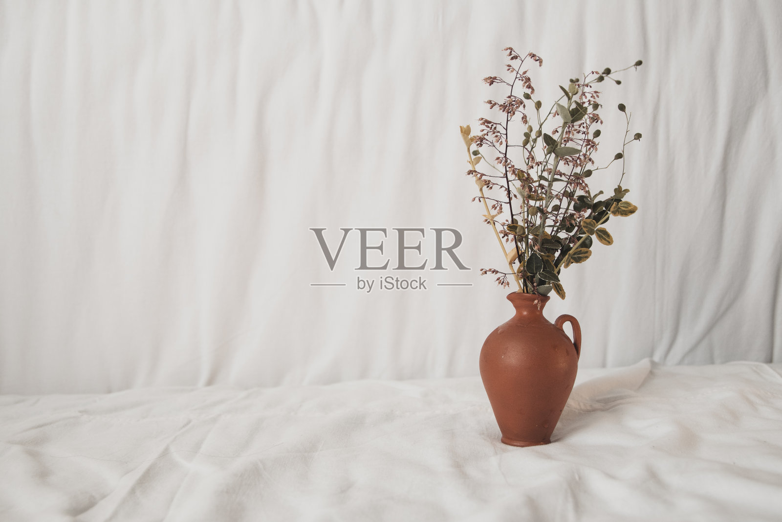 美丽的野花插花在时尚的粘土花瓶白色天然棉织物背景。照片摄影图片