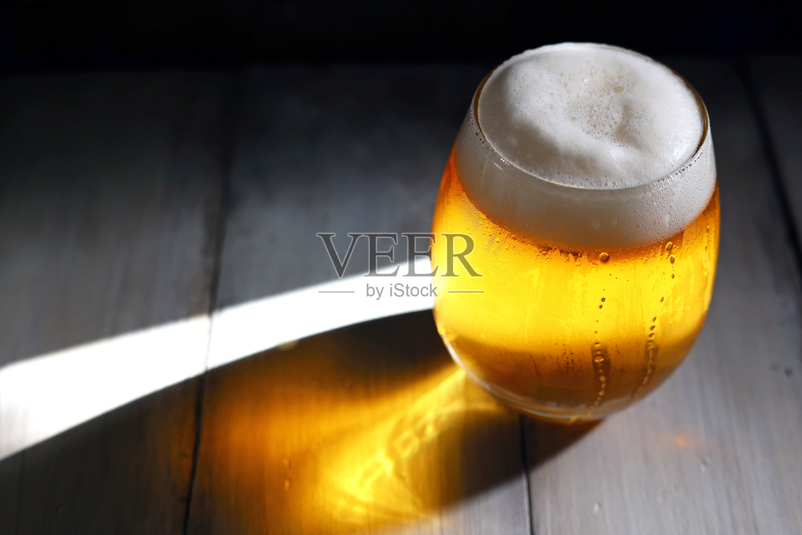 一杯充满泡沫的啤酒倒进一个短而圆的玻璃杯里，在午后强烈的阳光照射下熠熠发光照片摄影图片