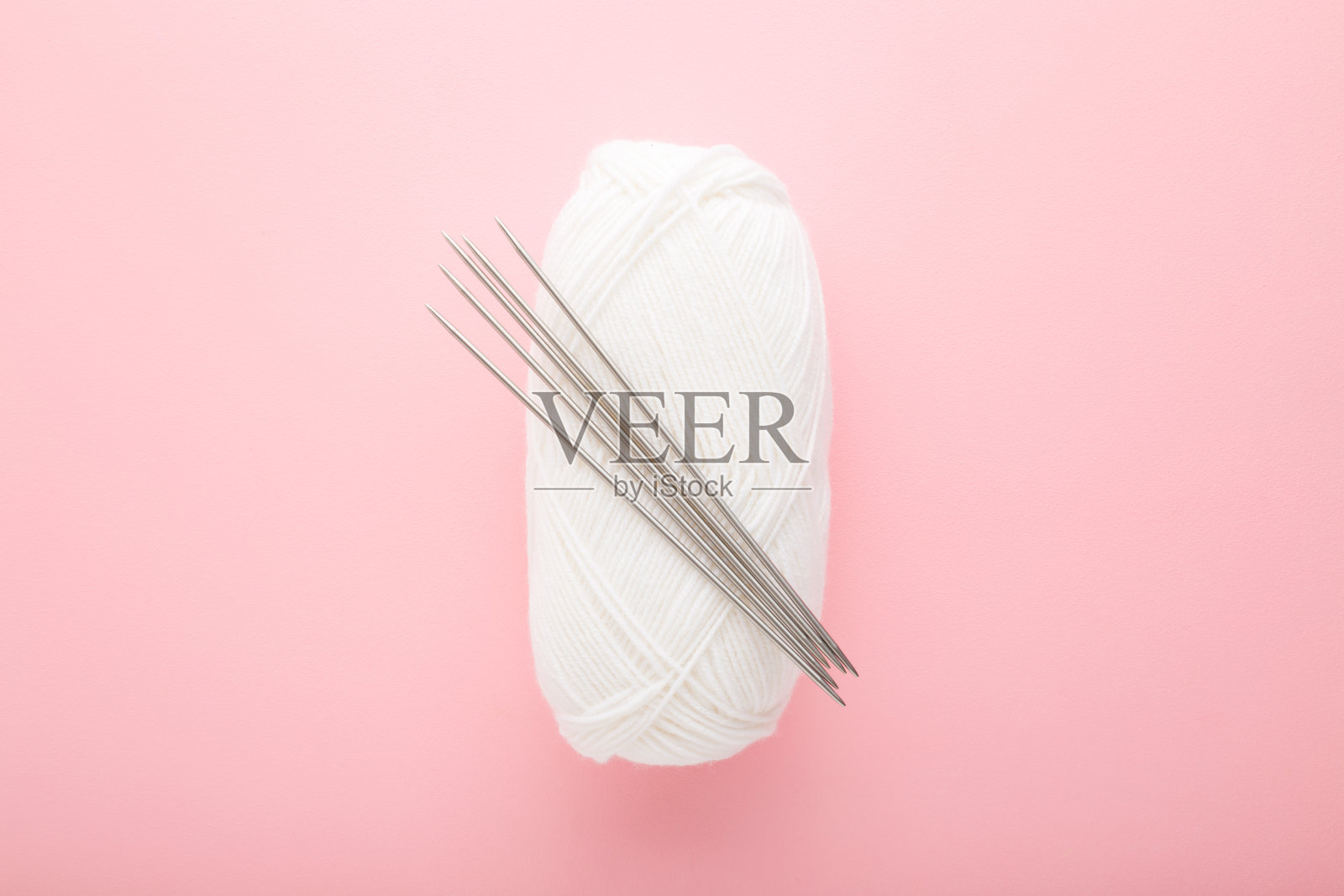 白色羊毛线和金属针，用来编织衣服或其他东西。浅粉色桌面背景。柔和的颜色。特写镜头。自顶向下的观点。照片摄影图片