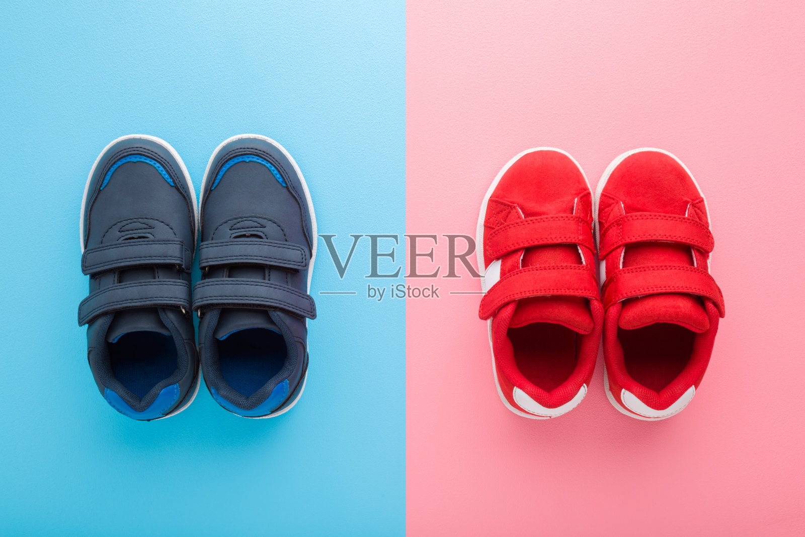 红色和深蓝色的运动鞋为小男孩和女孩在浅蓝色粉红色的桌子背景。柔和的颜色。儿童鞋。特写镜头。自顶向下的观点。照片摄影图片