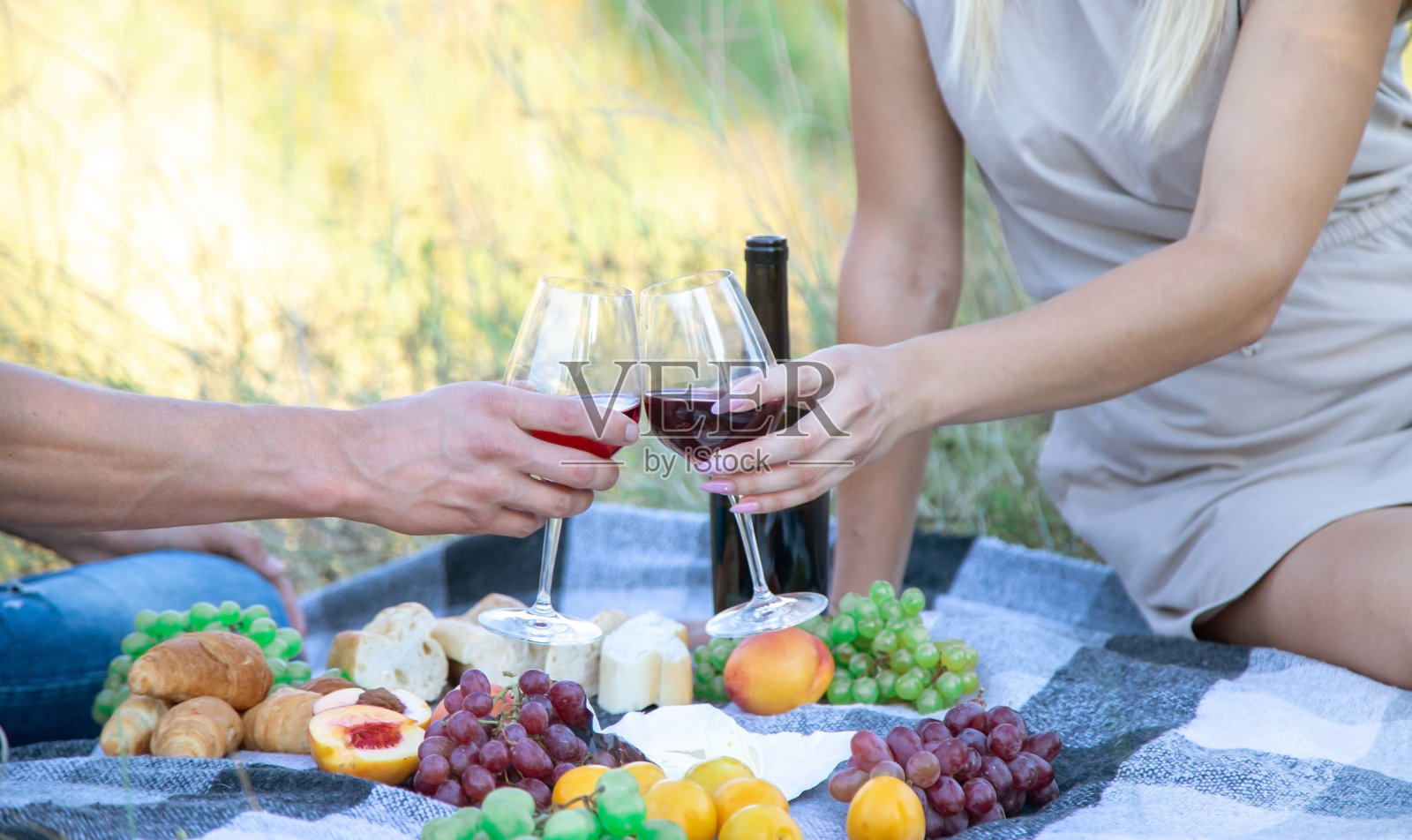 在大自然野餐时，一个女孩和一个男人正捧着盛着酒的酒杯。照片摄影图片