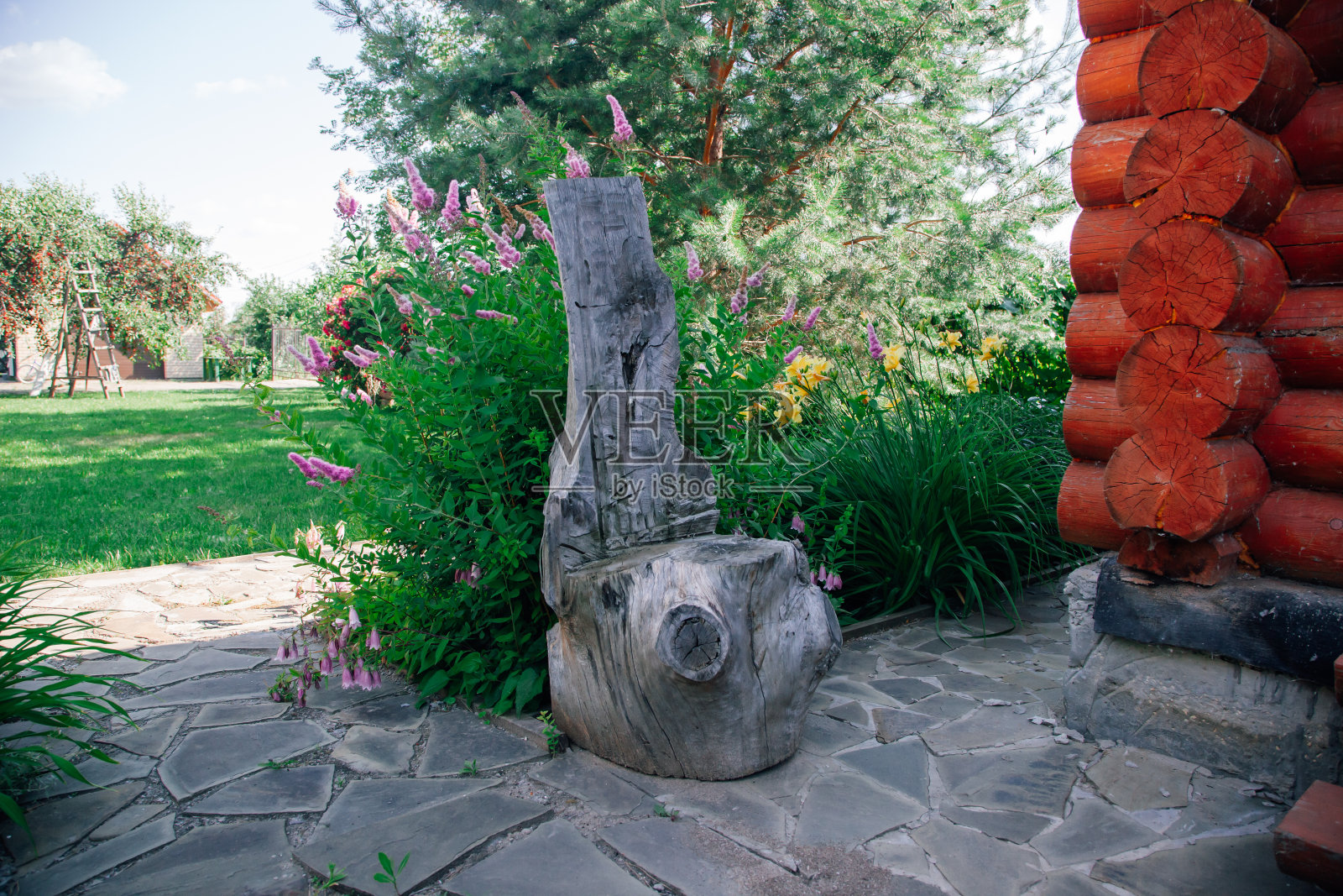 原木在垂直和水平切割的石头瓷砖路面附近的木屋与花，绿色植物和树木的背景。乡村生活照片摄影图片