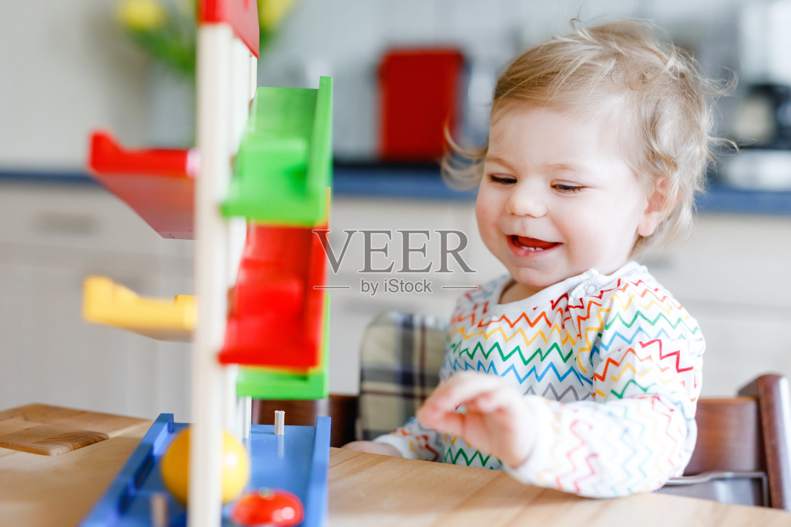 小女婴在家里或托儿所玩教育玩具。快乐健康的幼童与彩色的木制玩具球轨道乐趣。孩子们正在学习握球和滚球。肌肉运动的教育。照片摄影图片