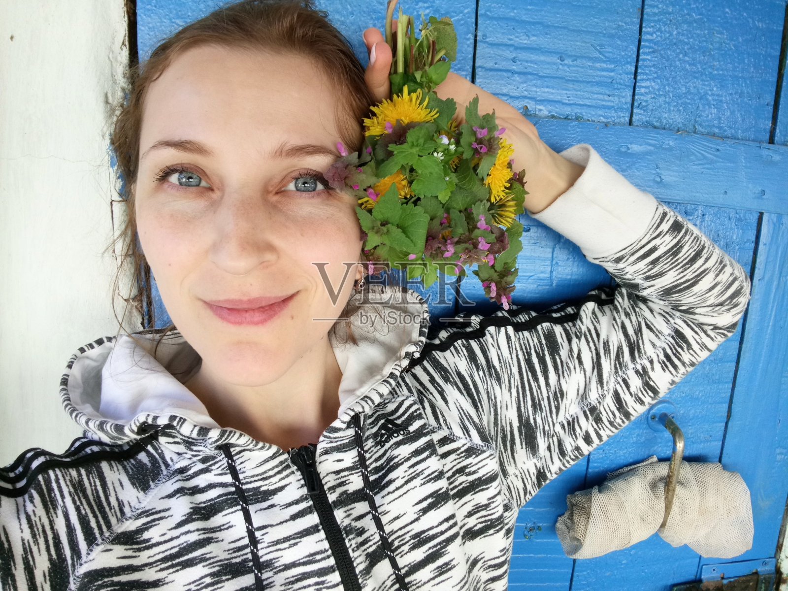 女孩看着镜头，拿着一束野花，背景是一扇蓝色的木门。照片摄影图片