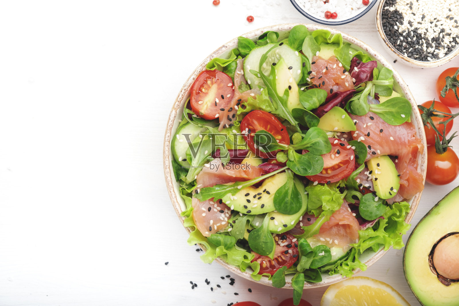 春季沙拉，腌鲑鱼，鳄梨，番茄，黄瓜，黑芝麻，橄榄油，混合香草。白色背景，顶部视图，复制空间照片摄影图片
