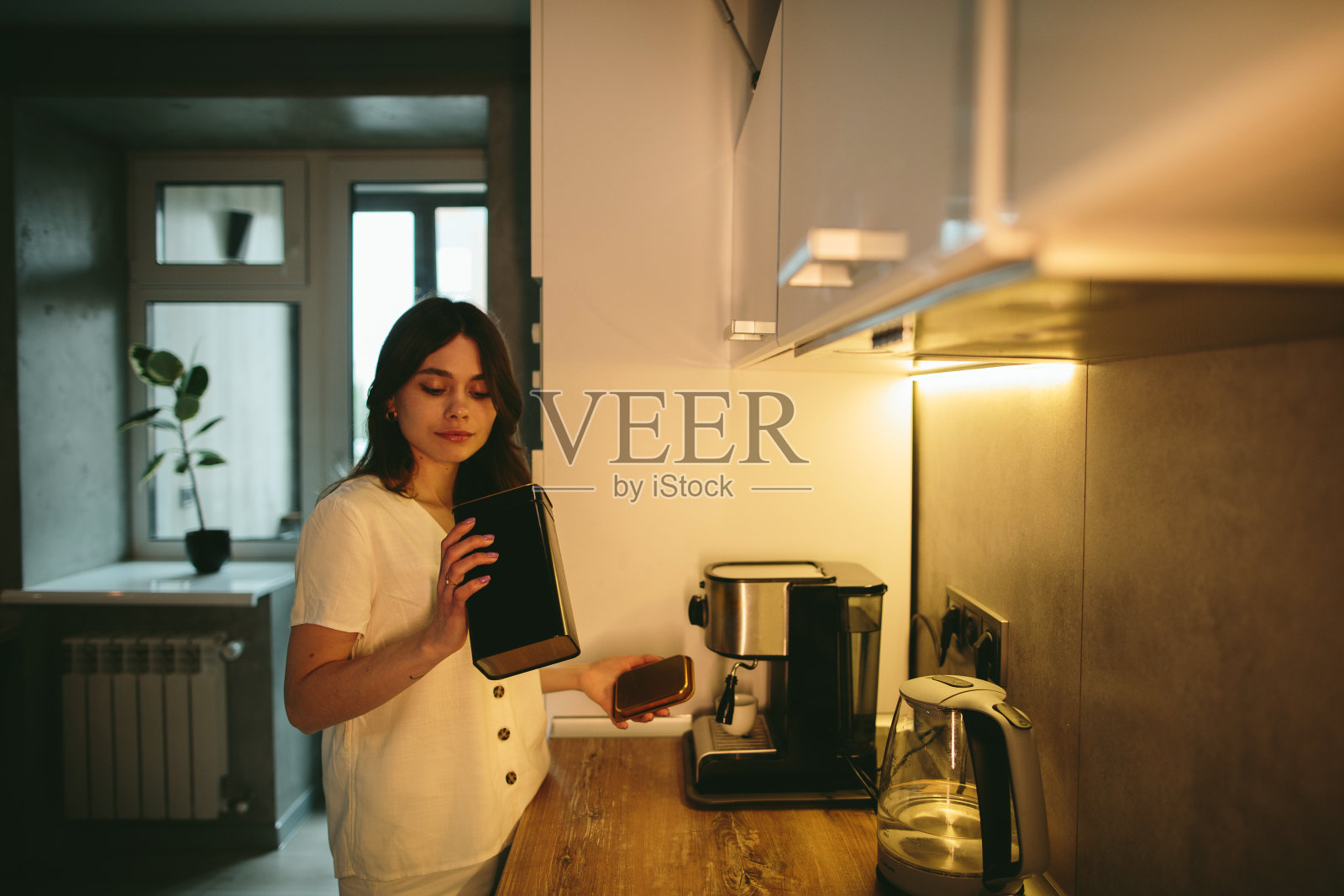 年轻的女人在厨房里煮咖啡。照片摄影图片